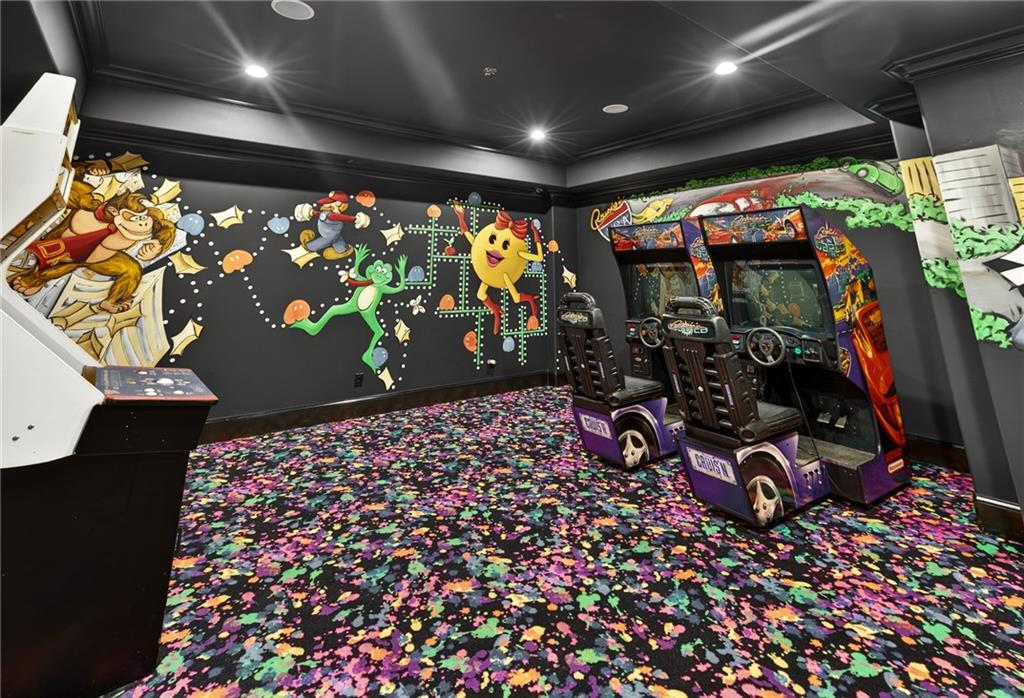 The game room features bold, colorful arcade-style décor with mural-covered walls and vibrant, patterned carpeting that gives the space a playful, retro atmosphere. 