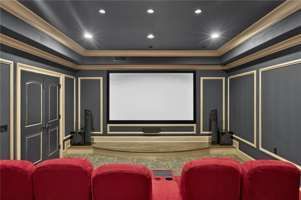 Rows of plush red theater seating face the screen, while dark walls with decorative paneling help enhance the cinematic setting.