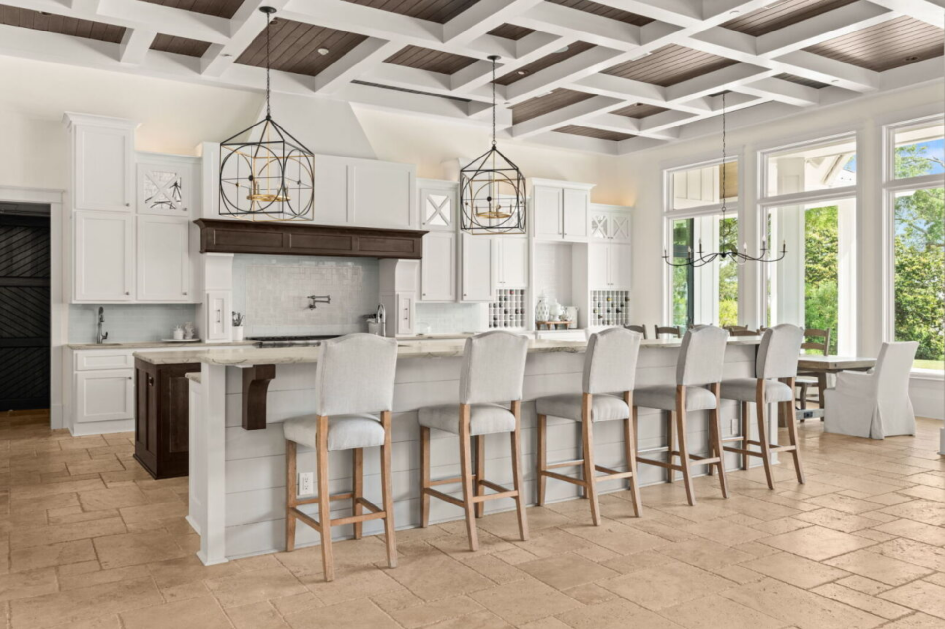 At the center, a large marble-topped island with dark wood cabinetry provides additional prep space and storage, along with a built-in sink and open shelving for cookware.