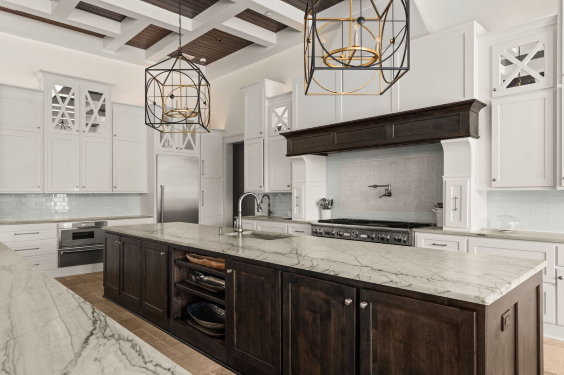 Past the two islands, a professional-grade Thermador range is set beneath a custom hood, surrounded by white cabinetry that stretches to the ceiling for additional storage. 