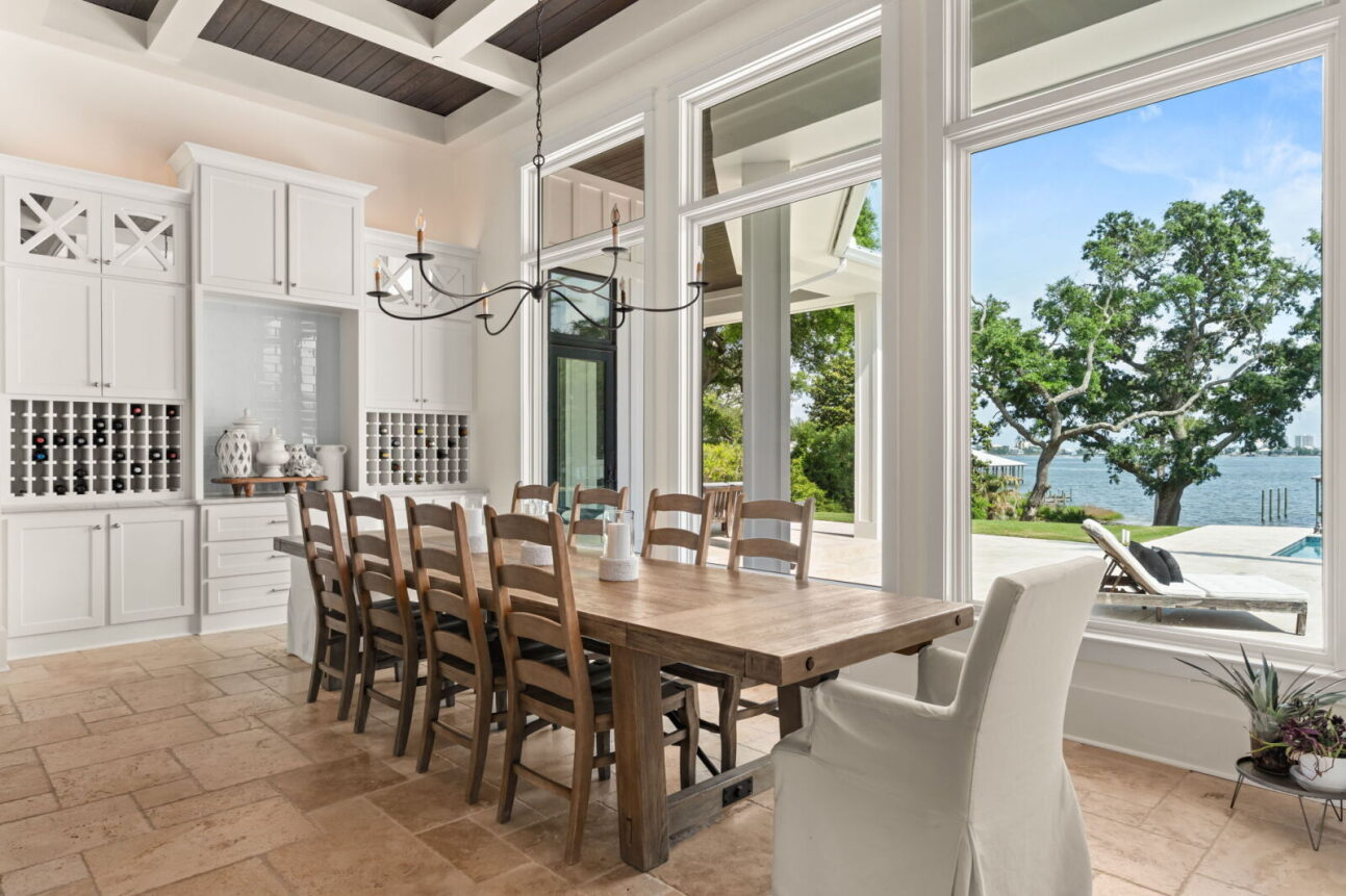 A long wood dining table sits beneath a simple iron chandelier, creating a warm gathering space framed by the same coffered ceiling that continues from the kitchen.