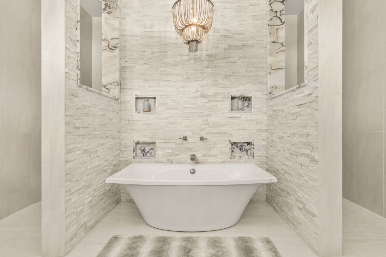 The primary bathroom carries a bright, spa-inspired palette with textured stone tile running up the walls behind a freestanding soaking tub. 