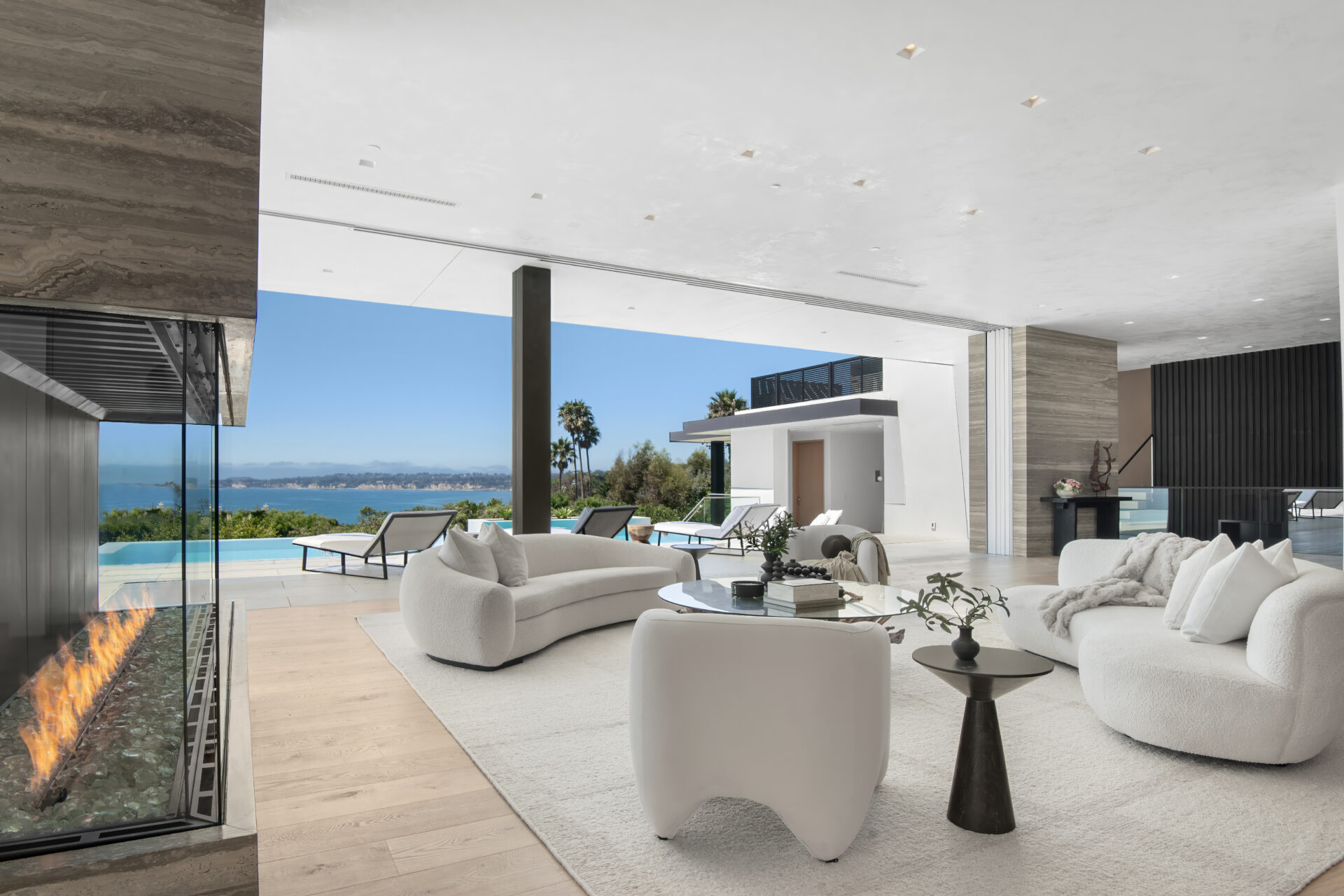 Above, the high ceilings keep the space feeling broad, while disappearing glass sliders open fully into stone pocket walls and extend the room toward the ocean-facing patio.