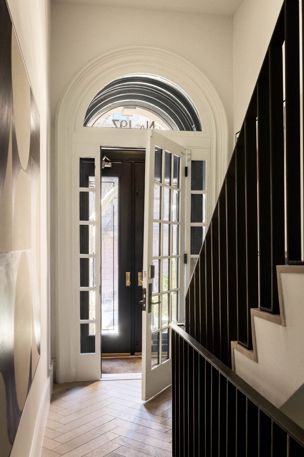 The traditional brownstone entry opens through a set of glass-paneled doors beneath an arched transom, bringing natural light into a narrow hall leading to the parlor level.