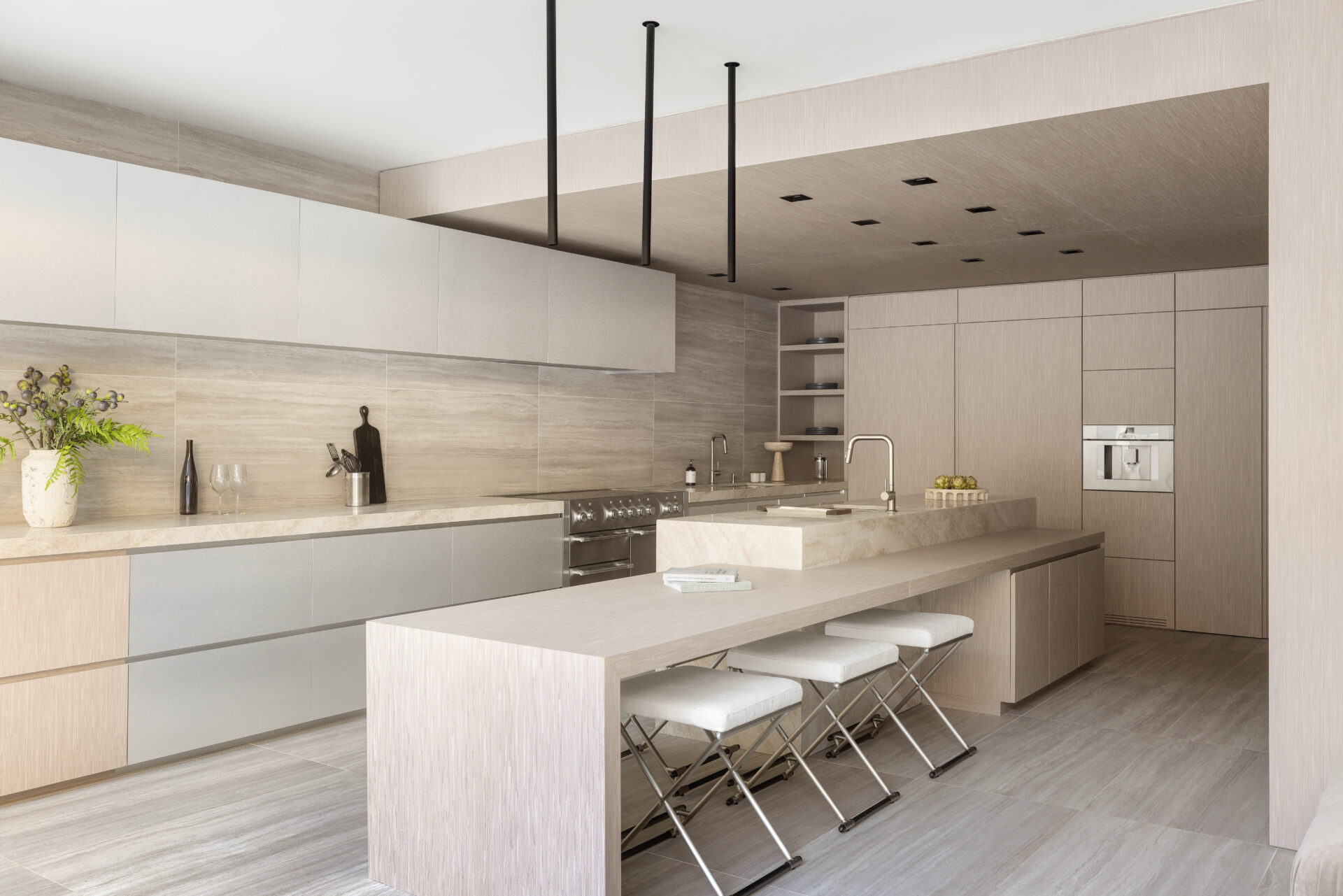 The kitchen itself is organized around a large central island, with a second built-in counter that extends outward as a dining ledge with folding stools tucked beneath it.