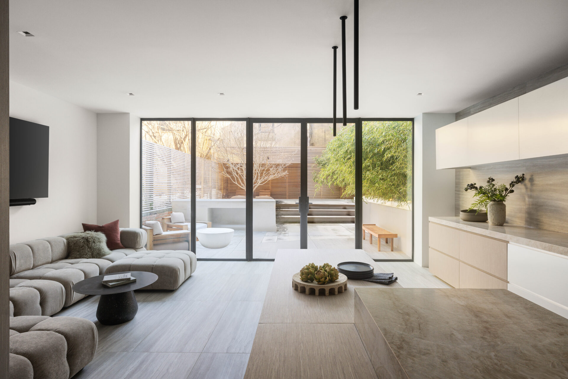 Off to the side, the lounge continues that same restrained palette but softens it with low, sculptural seating and a more casual arrangement facing the glass doors.