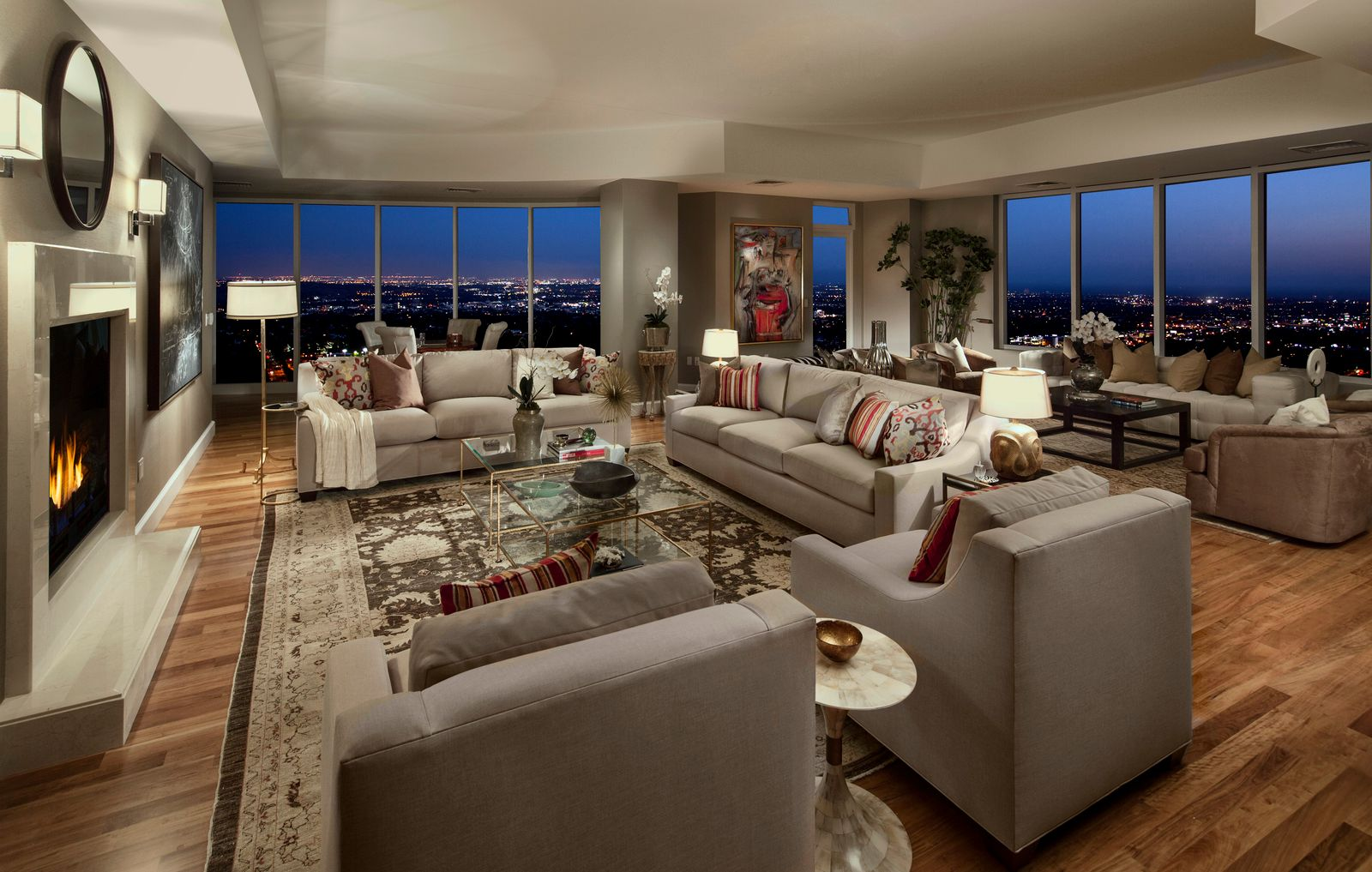 The walls of glass turn the city lights into the room’s backdrop, giving the entire space a soft glow that plays off the neutral furniture, warm wood floors, and layered lighting.