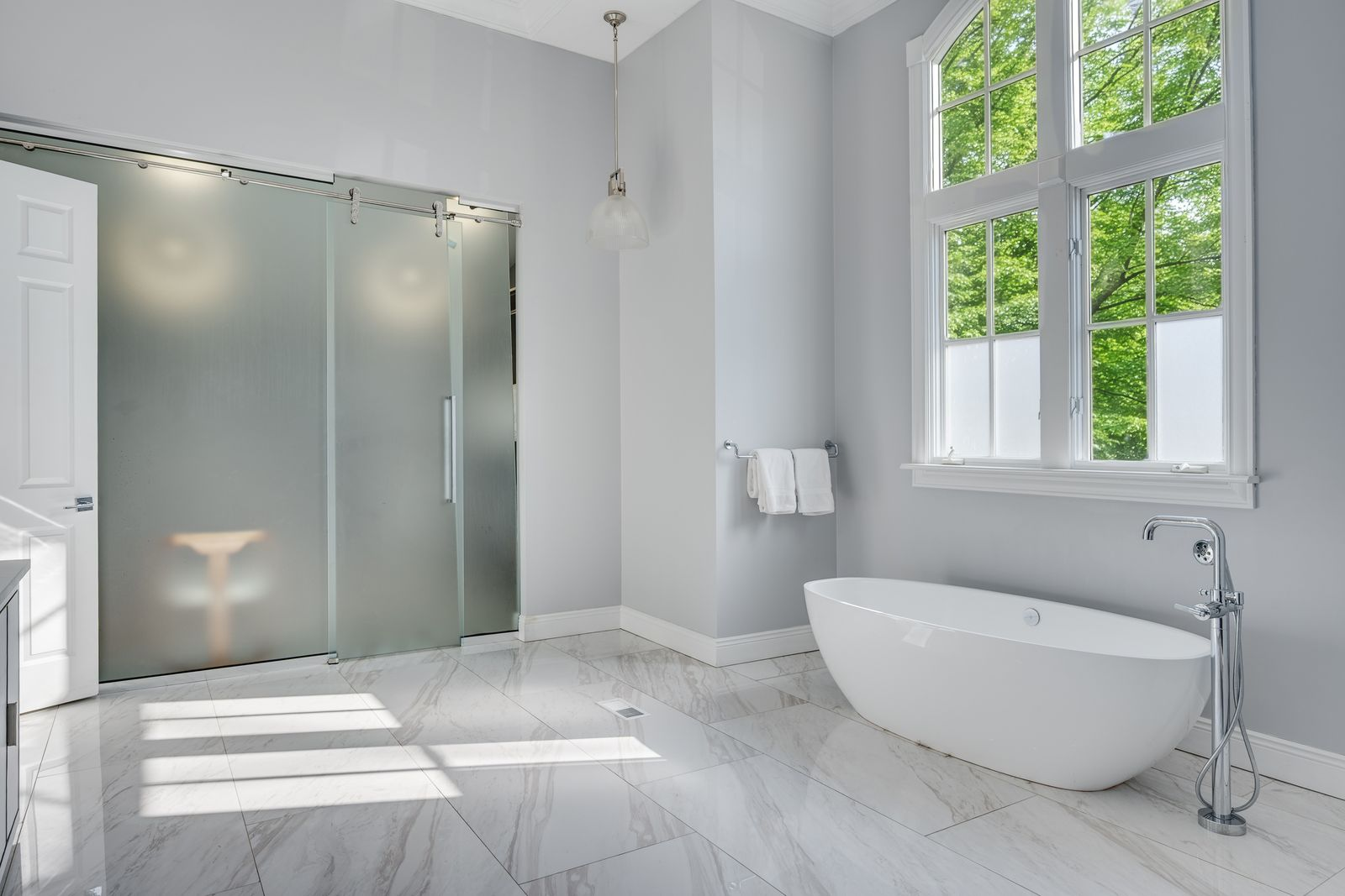 The suite's bathroom continues that airy look with tall windows, pale walls, and a freestanding soaking tub set beneath the glass. 