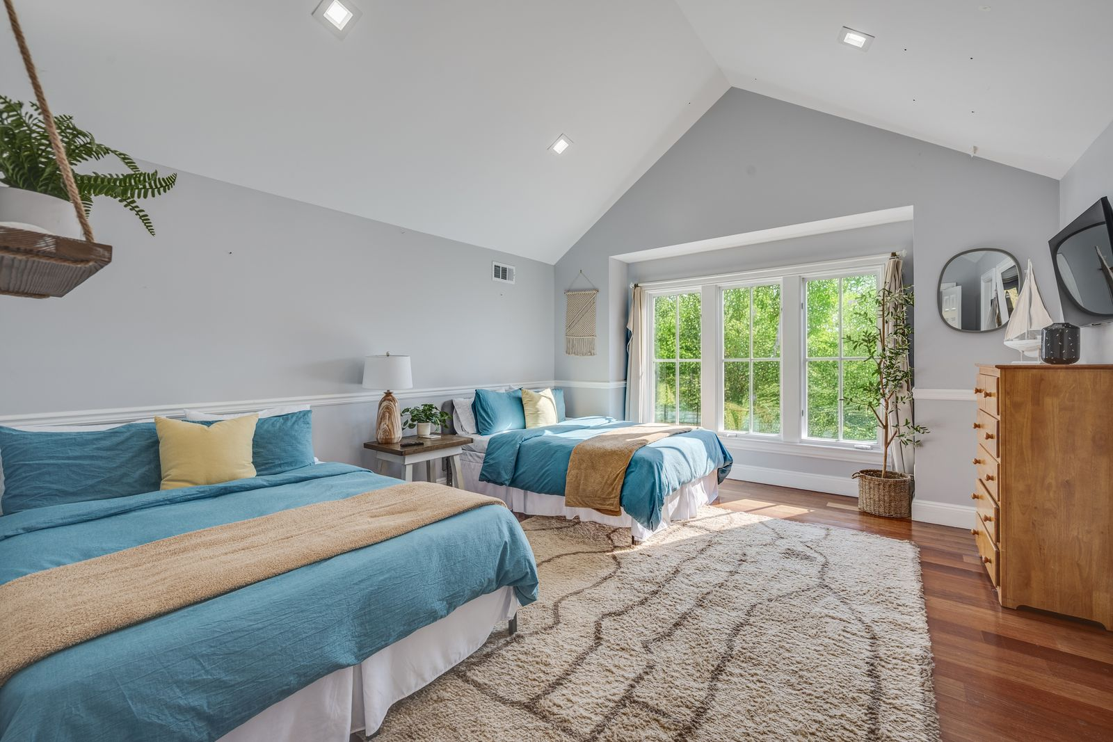 Down the hall, this guest bedroom keeps the same bright, airy look as the rest of the upper level, with a vaulted ceiling that lifts the room and a deep window alcove pulling in greenery from the trees. 