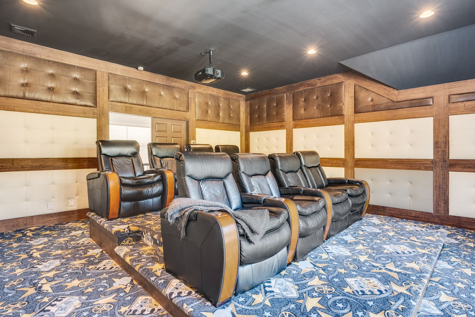 The finished lower level includes a dedicated movie theater designed with a traditional screening-room layout, centered around two raised rows of oversized leather recliners facing a projector. 