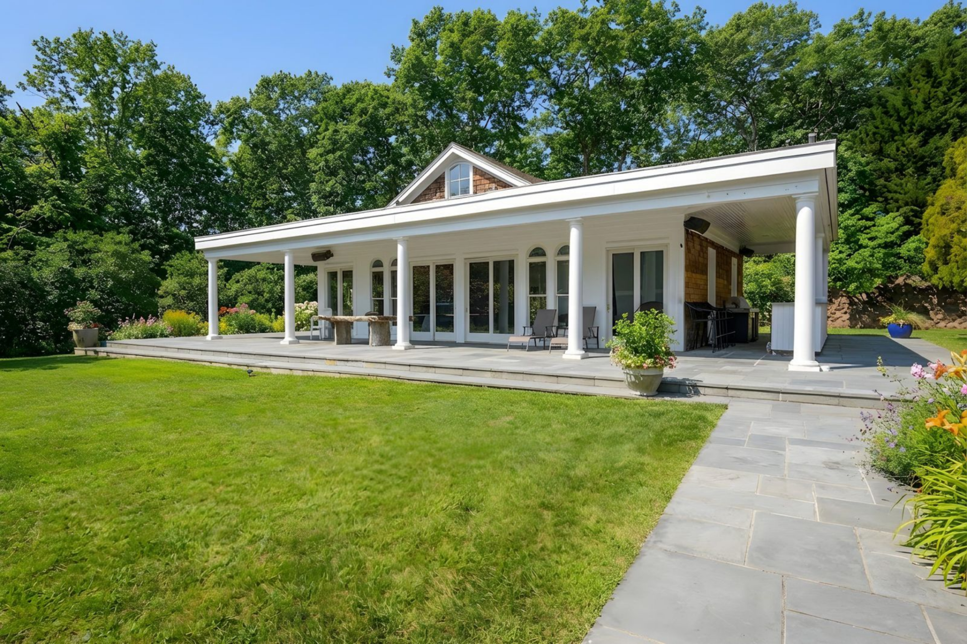 Set off to the side, the pool house is designed as its own entertaining pavilion, with a long covered terrace supported by white columns wrapping around the structure. 