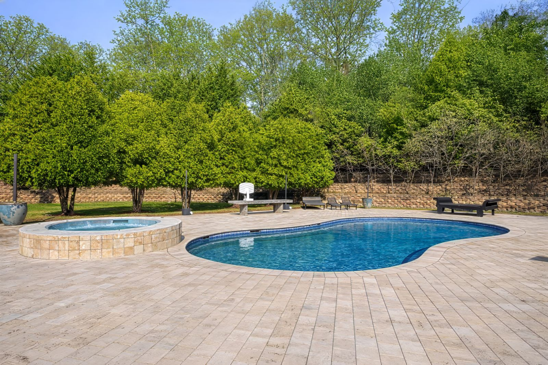The pool has a soft, curved outline, paired with a raised circular spa and surrounded by plenty of deck space for seating.