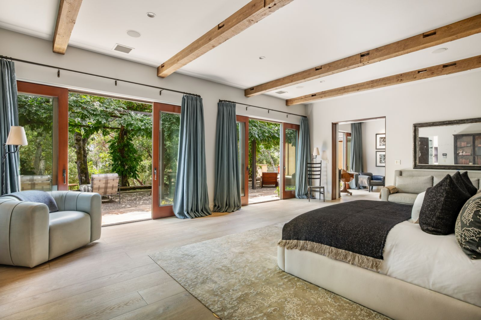 A low upholstered bed anchors the room, while a pair of curved lounge chairs and long drapery panels soften the edges and keep the space feeling open rather than crowded.