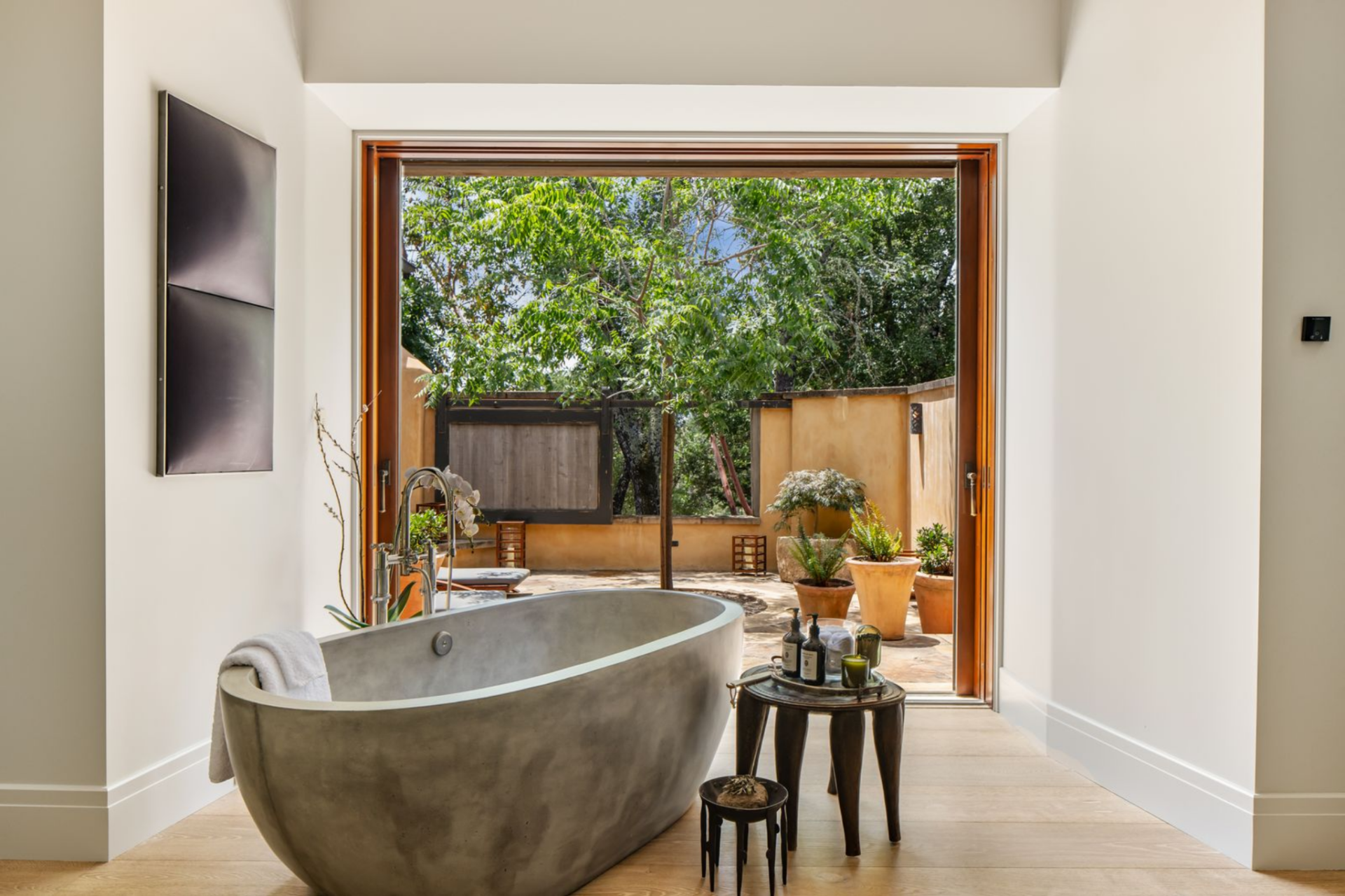 Freestanding soaking tub sitting in front of an open doorway that connects to a private outdoor patio.