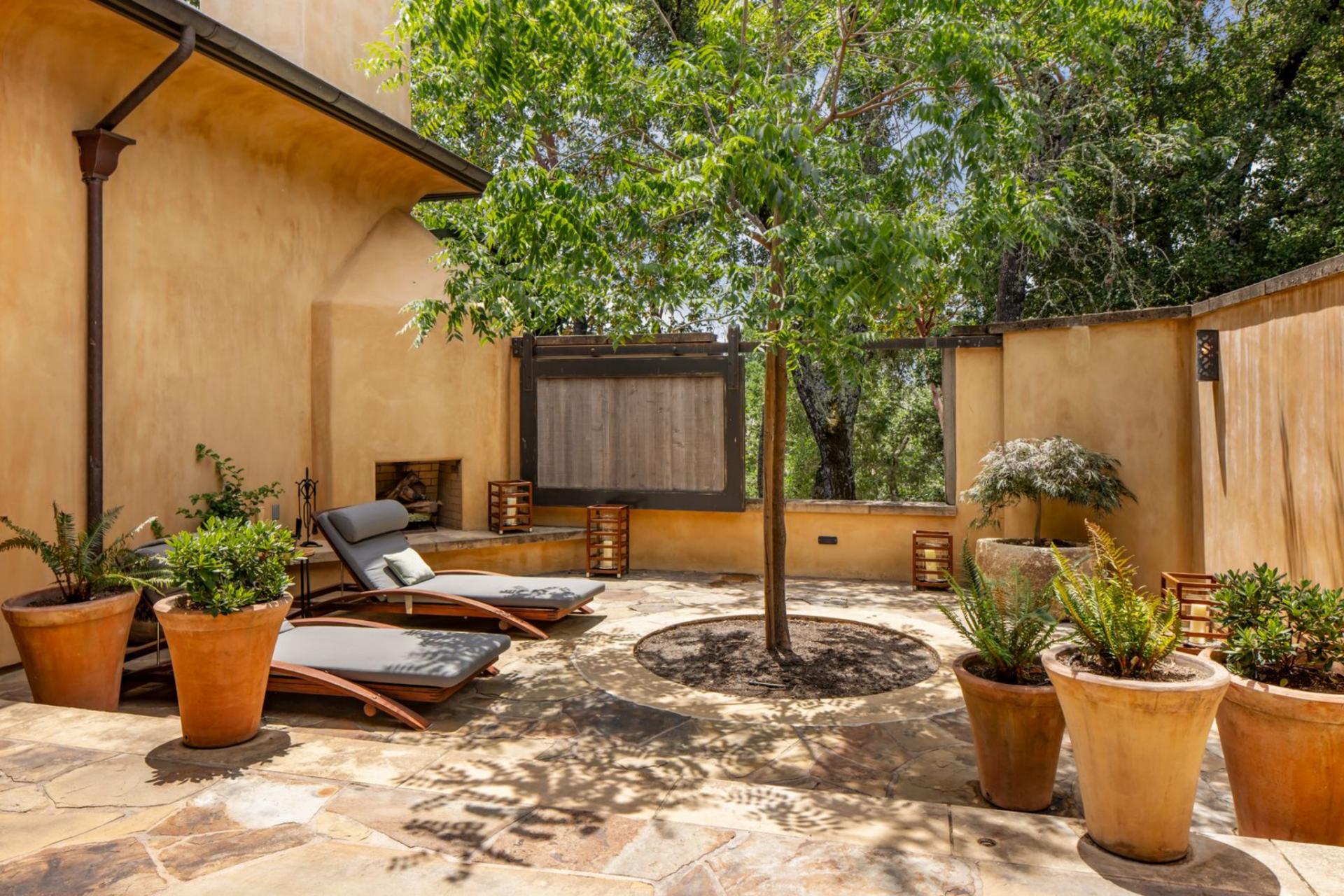 Right behind the bathtub, the suite opens to a private terrace enclosed by warm-toned stucco walls and planted with potted greenery around the edges. 