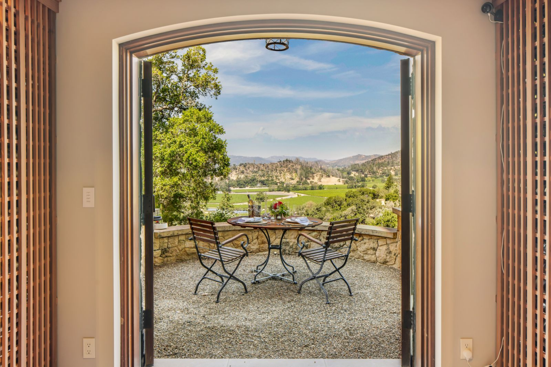 At the back, arched doors open directly to a compact tasting patio, where a small bistro table is positioned against a low stone wall overlooking the valley and vineyards below.