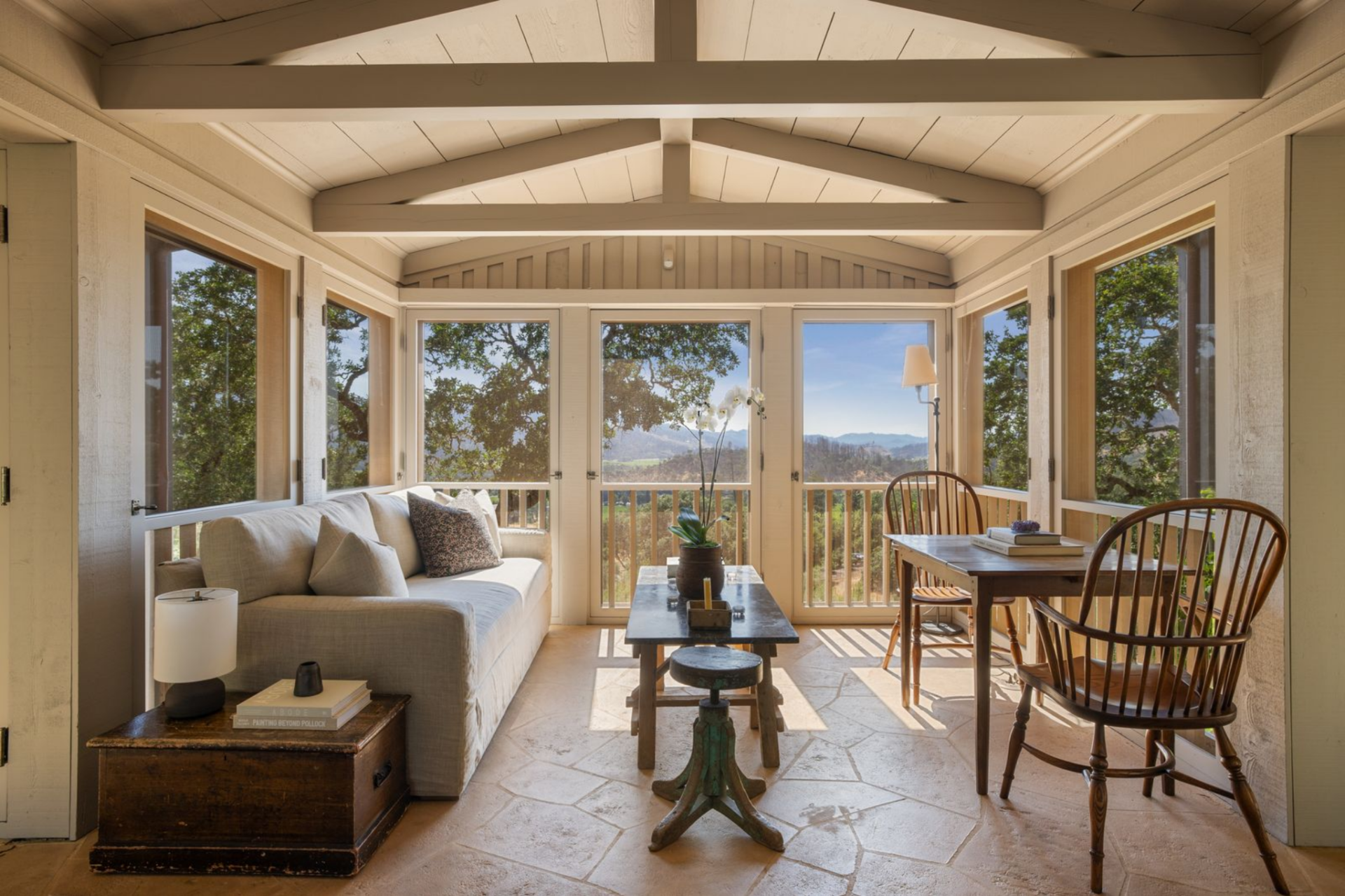 Exposed beams run across the ceiling, while a sofa and compact dining table are arranged around a central coffee table, keeping the layout tight and proportional to the room.