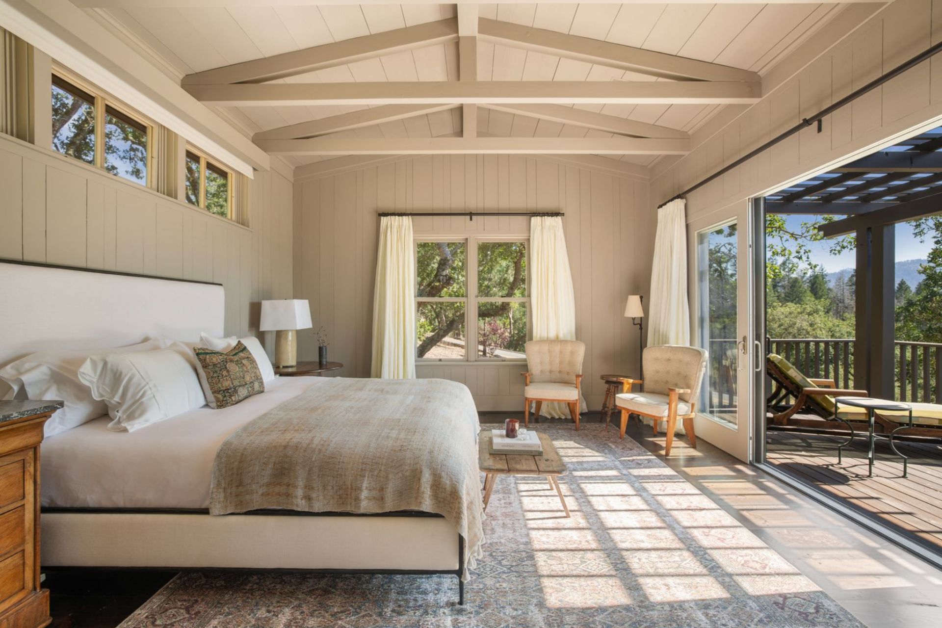 The bedroom is positioned at the end of the cottage, with a bed centered along one wall and a pair of chairs placed near the sliding glass doors that open directly to a private deck.