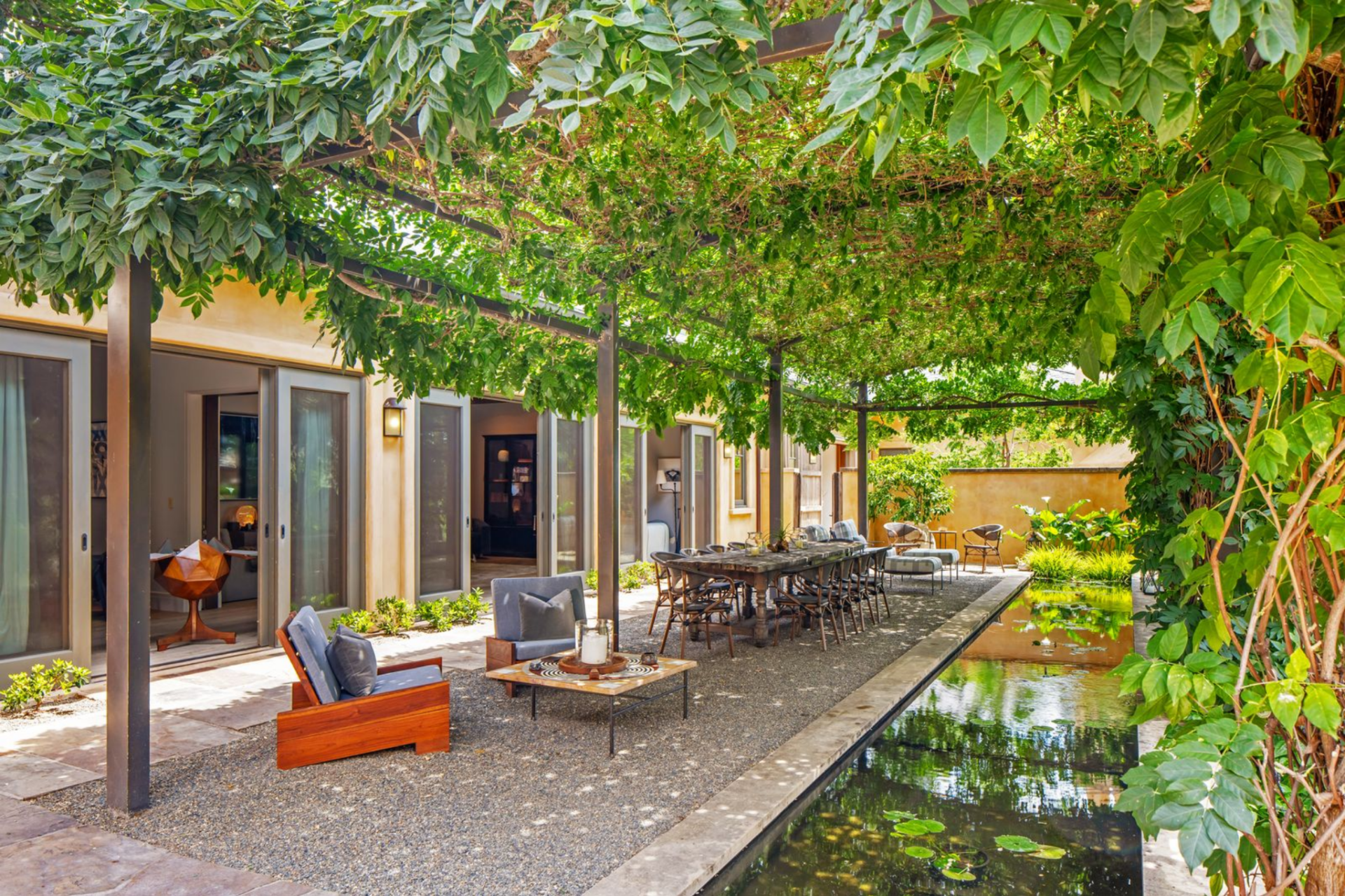 Just off the primary suite, a covered dining terrace sits beneath a pergola wrapped in greenery, creating a shaded extension of the interior. 
