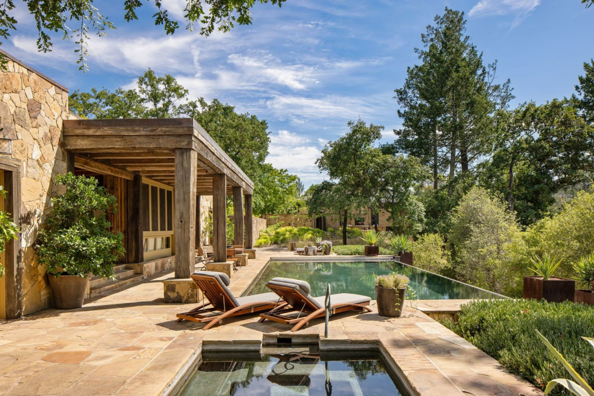Positioned along a stone terrace, the infinity edge pool drops toward the landscape, allowing the waterline to visually merge with the horizon, while a raised spa sits just behind a pair of lounge chairs.