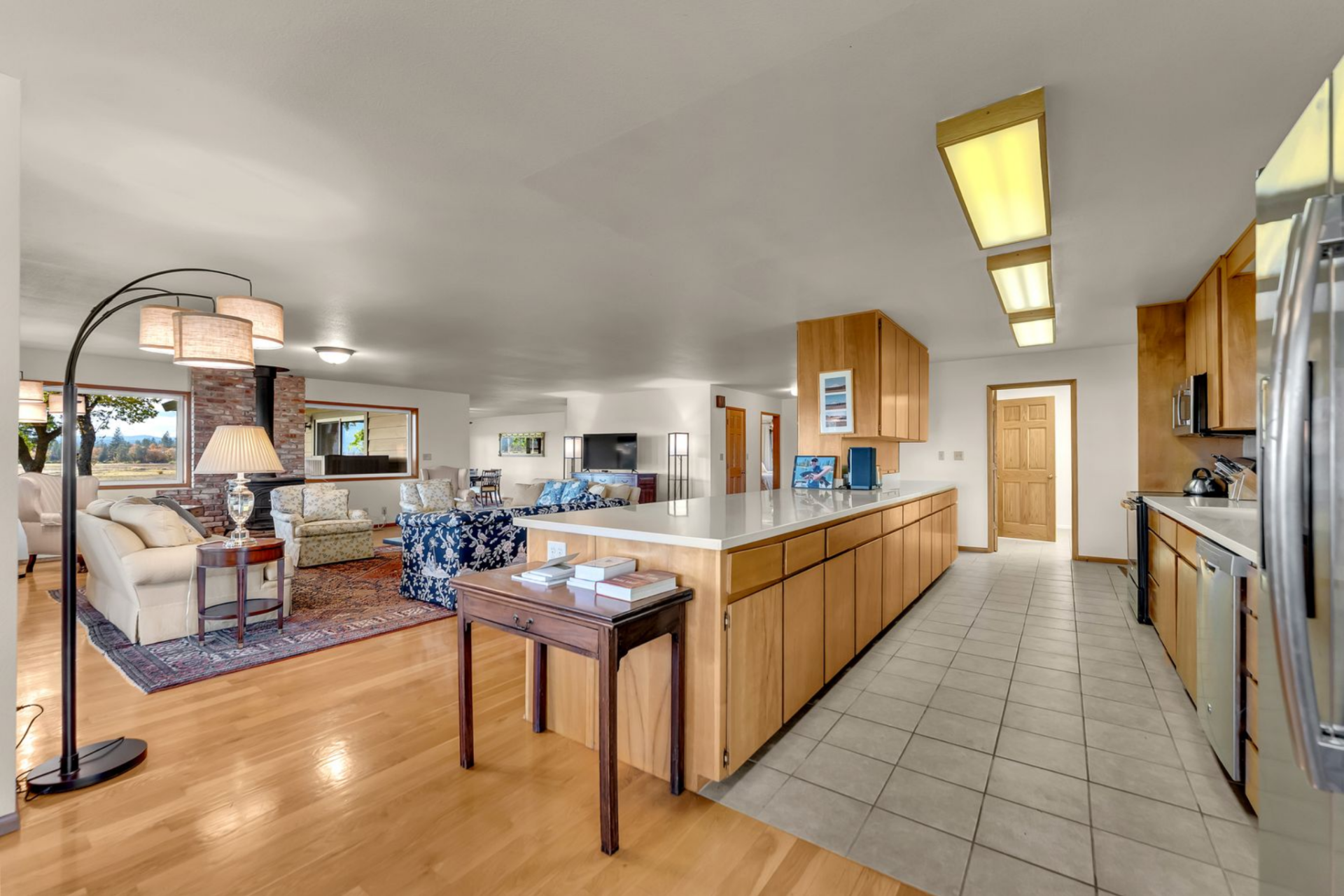 Wood cabinetry lines both sides, white countertops brighten the layout, and the floor shifts from hardwood to square tile, marking the kitchen as its own zone.