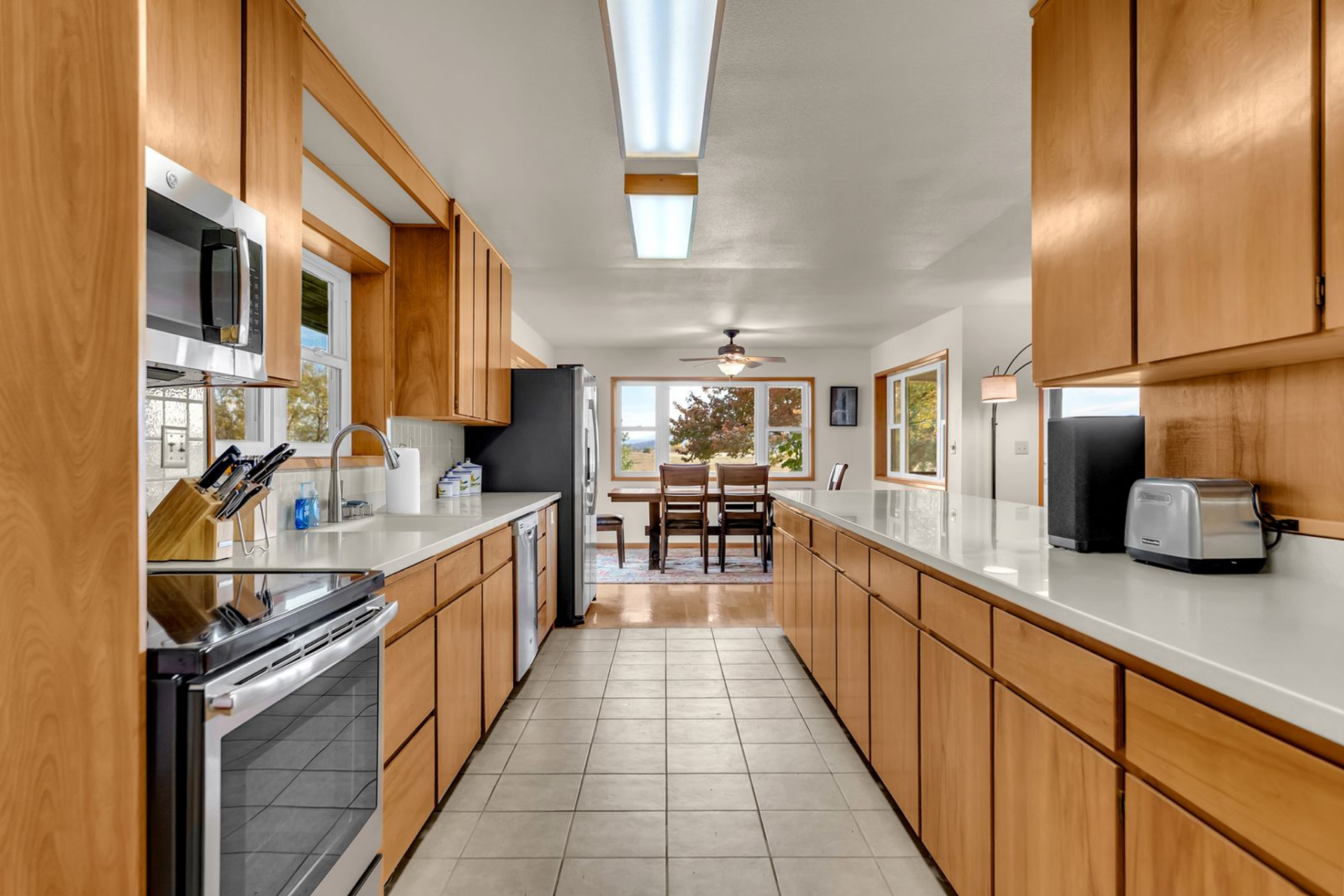 One side holds the main work area with the sink, range, and upper cabinetry, while the opposite side is almost entirely given over to the extra-long counter, creating a wide corridor through the middle of the room. 