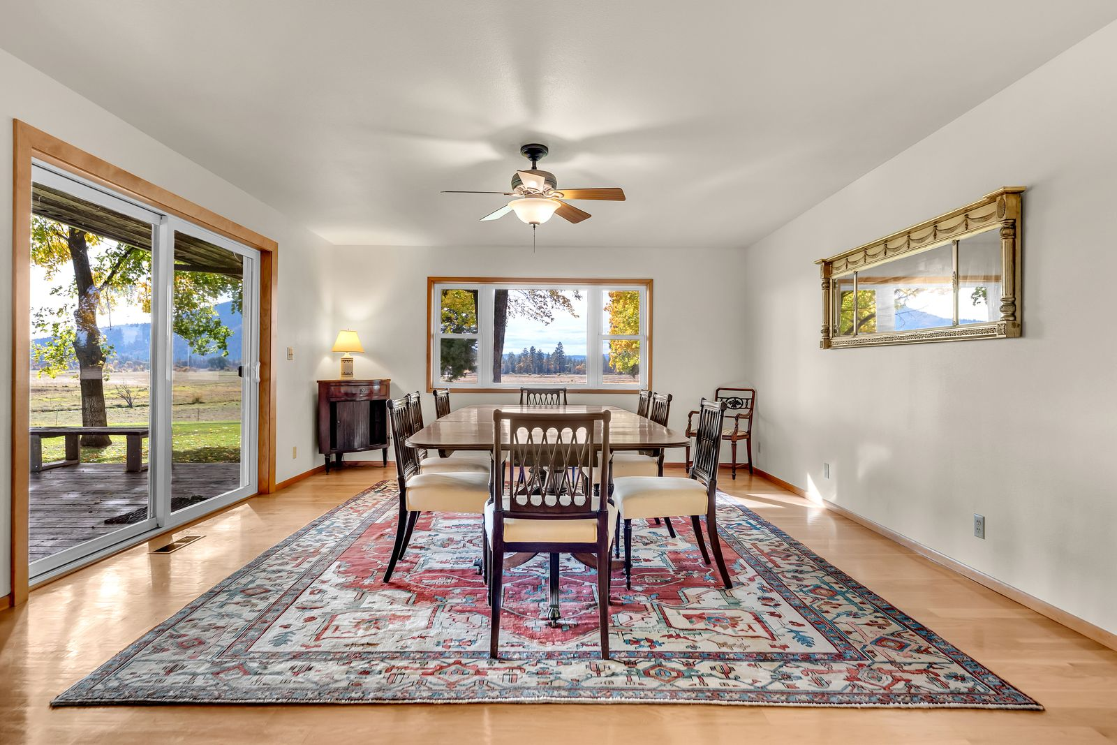 On the other side of the living room, the formal dining room opens with a long wood dining table surrounded by matching chairs centered over a large patterned rug. 