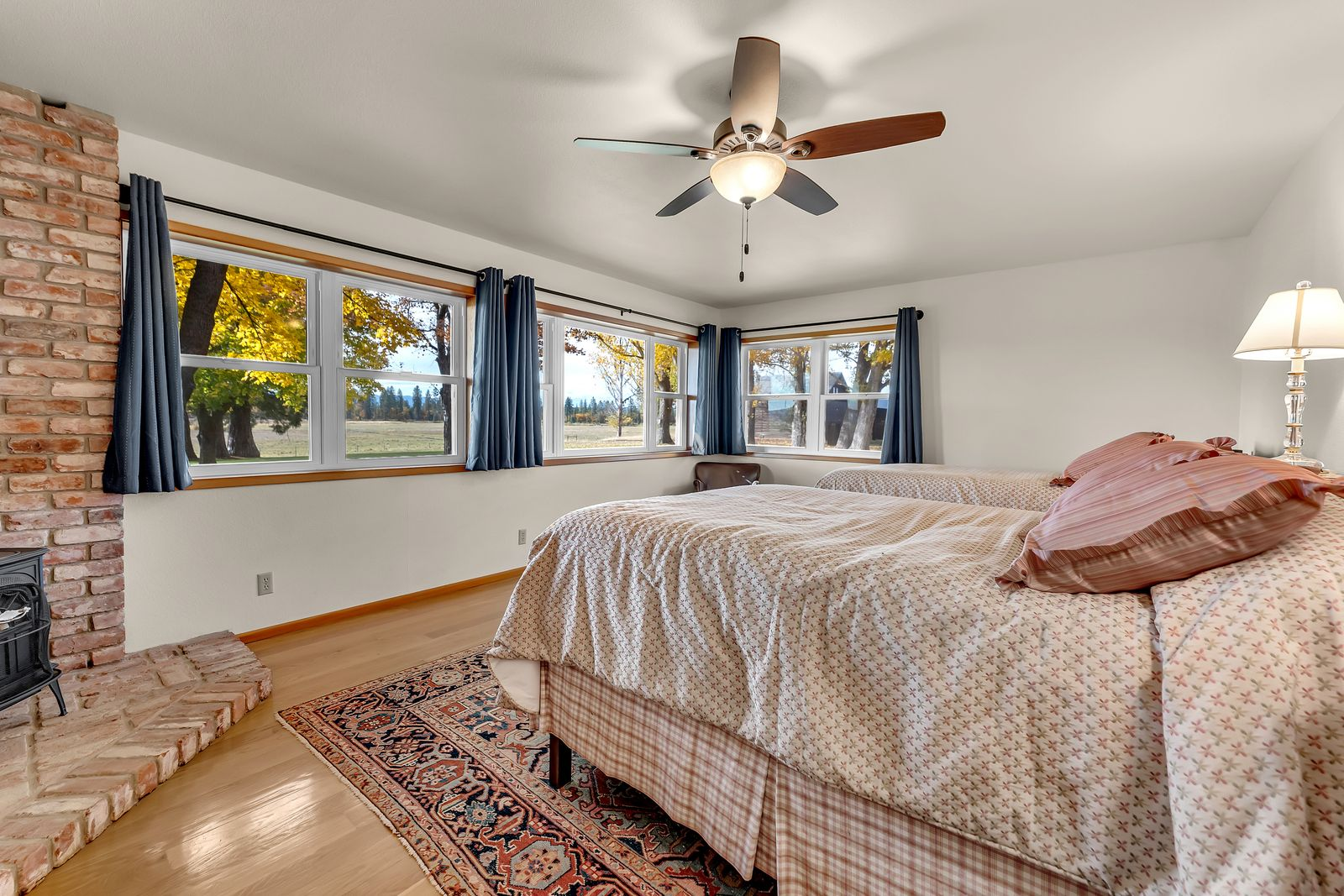 Two beds are positioned to face outward toward the windows, while blue drapery and warm wood trim frame each to add a bit of contrast against the simple palette.
