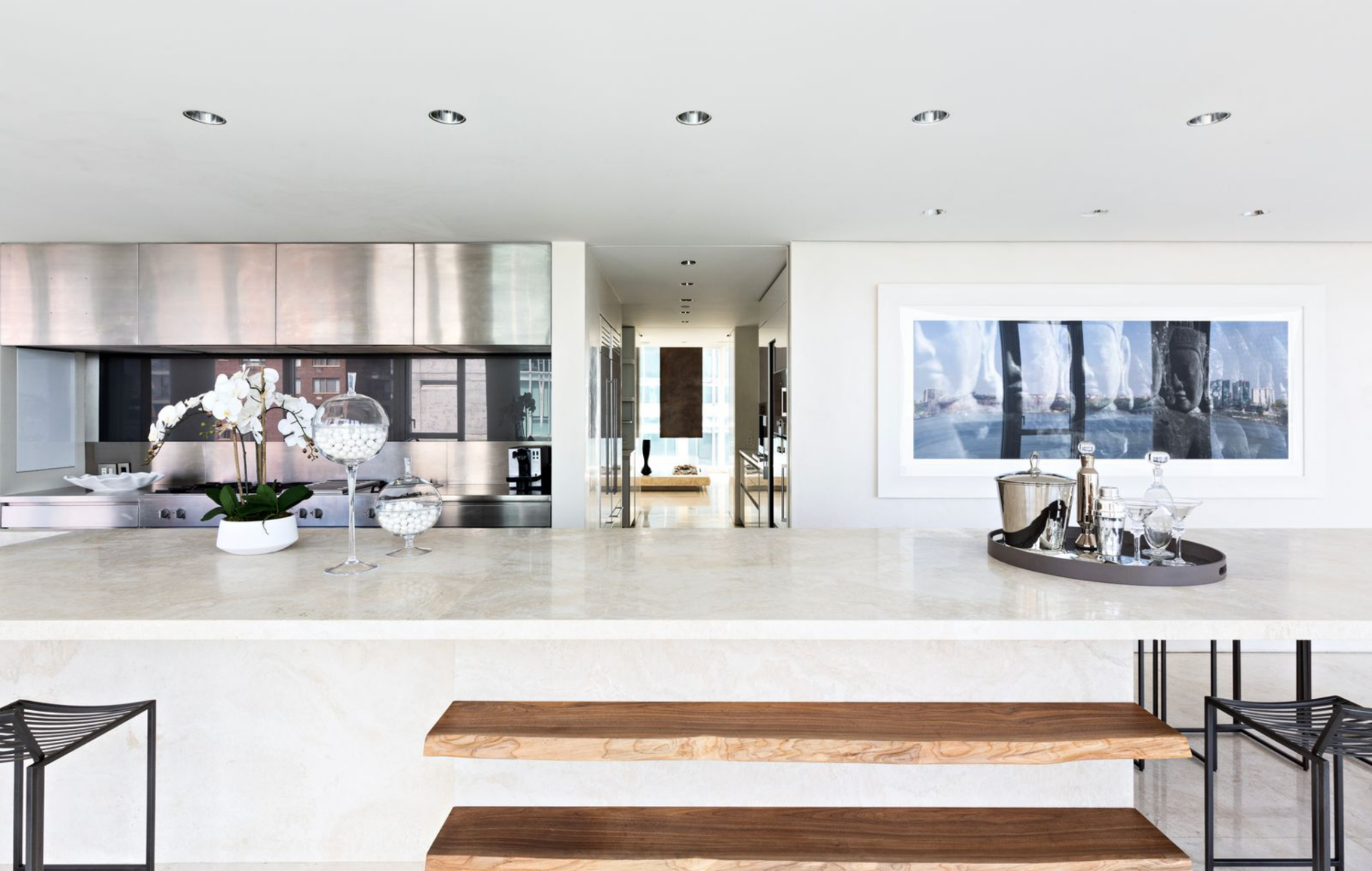 Across from it, the main cooking wall is finished almost entirely in stainless steel, with a long professional-grade range set beneath a matching hood and backsplash. 