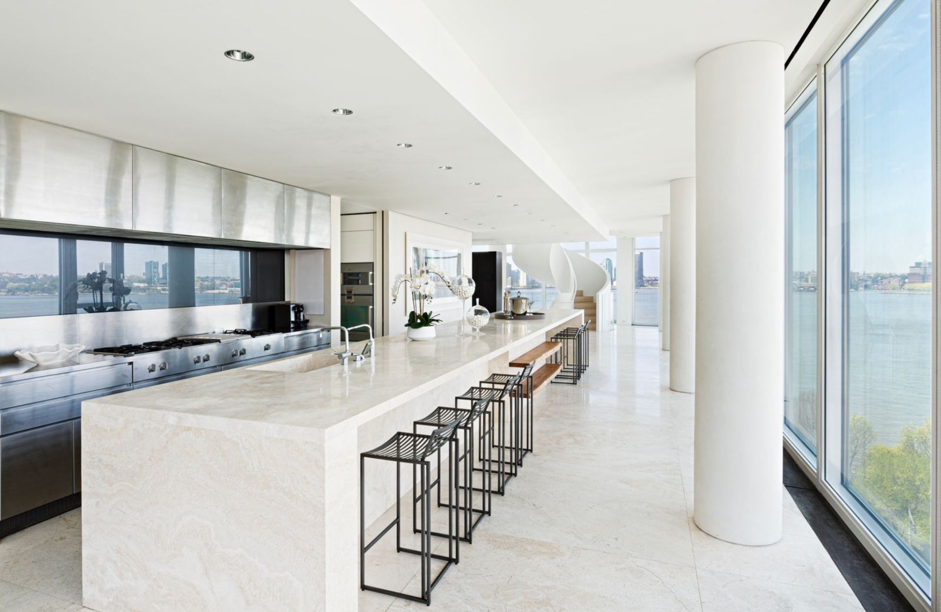 A small hallway off the dining gallery leads into the kitchen, where an oversized stone island stretches nearly the full length of the space with a sink at one end and a row of black-framed stools on the other.
