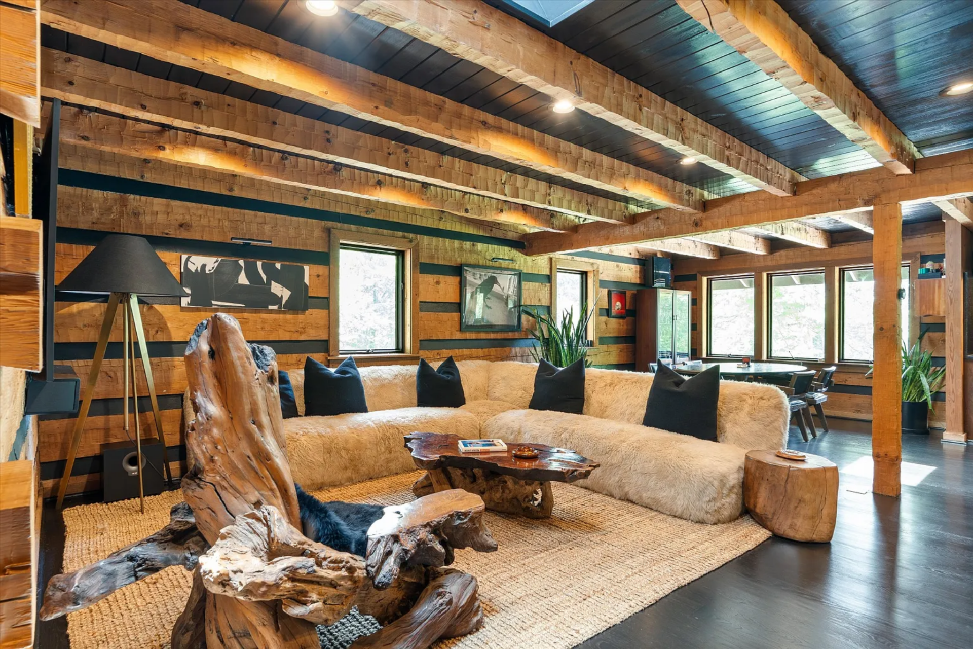 The walls are built from stacked hand-hewn logs with dark chinking between them, while the ceiling alternates between heavy natural beams and darker plank insets that emphasize the room’s low, sheltering profile.