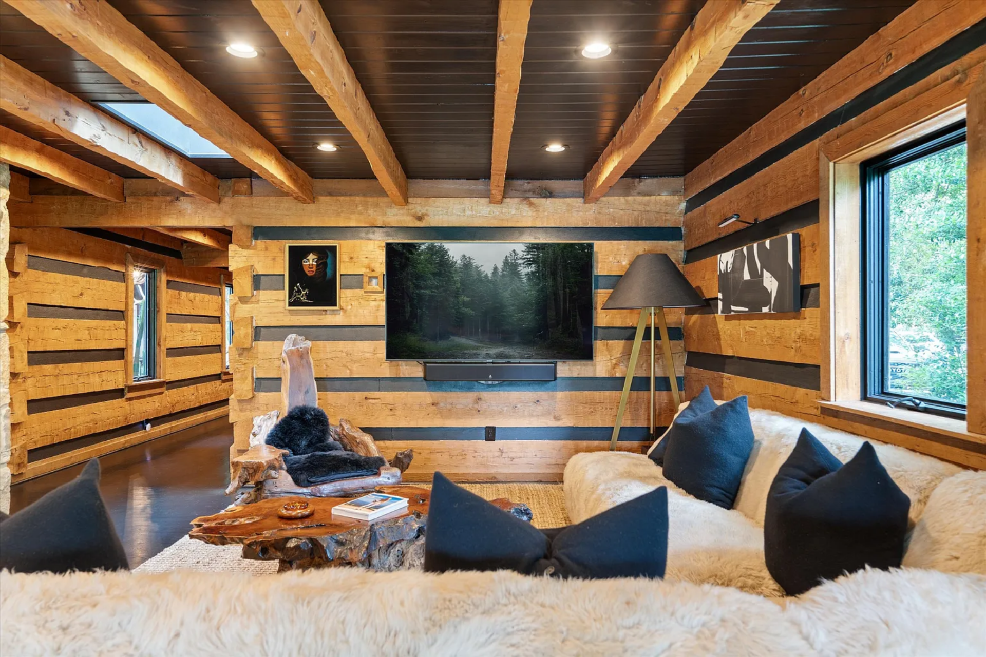The main seating area is arranged around a large sectional upholstered in a thick shearling-like fabric, with black accent pillows, a rough-hewn wood coffee table, and sculptural stump seating.