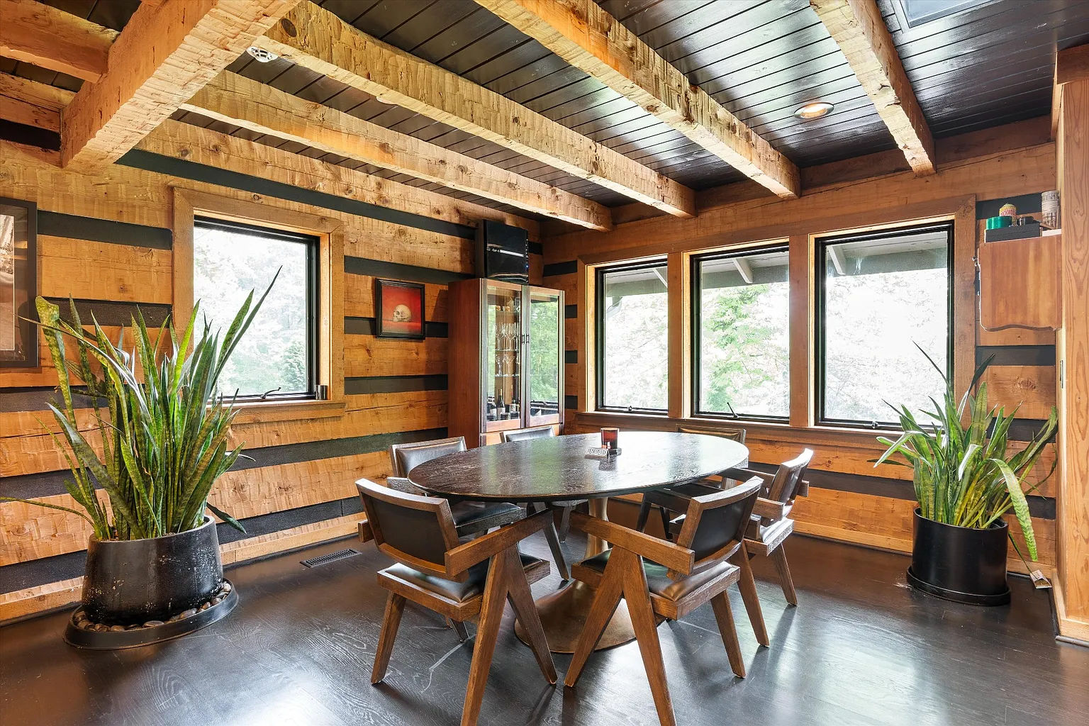 Behind the main seating area, the dining space features a round dark wood table surrounded by angular wood-and-leather chairs. 