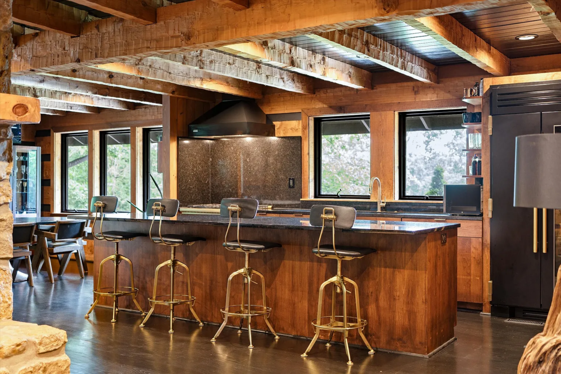 Open shelving, wood cabinetry, and a full-height refrigerator are integrated into the perimeter, and the island creates a natural divide between prep space and casual seating, keeping the kitchen open to the adjoining rooms while functioning as its own gathering point.