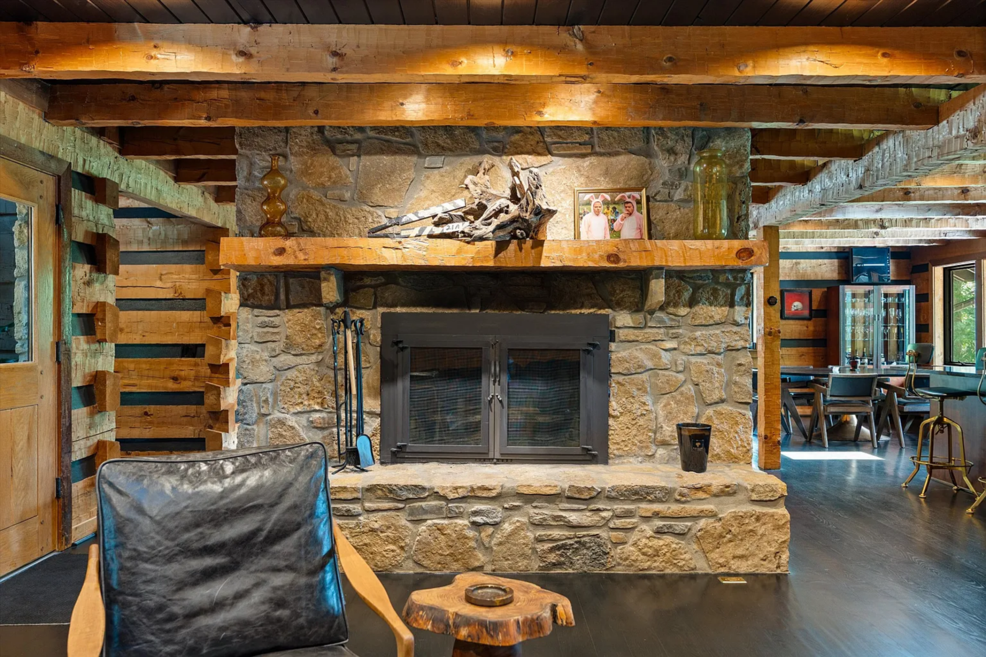 From the opposite angle, a full stone fireplace comes into view at the center of the room, framed by a thick timber mantel and rough-cut masonry. 