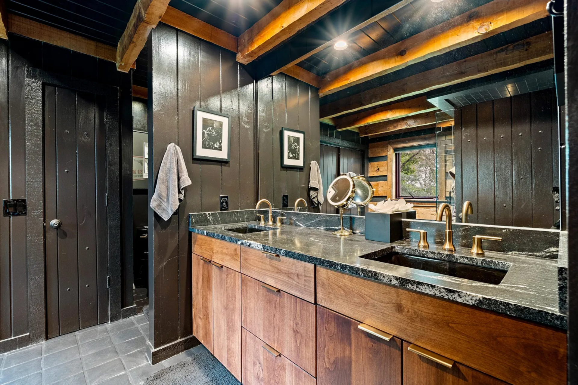 From there, the suite opens into an en-suite bathroom where a long double vanity with wood cabinetry and a stone countertop runs along one wall, fitted with two rectangular sinks and brass fixtures.