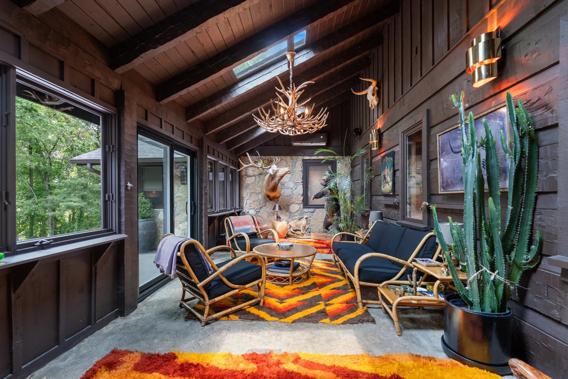 A grouping of rattan seating is arranged around a round glass-topped table, with bold patterned rugs defining the center of the room and adding a strong hit of color against the darker finishes.