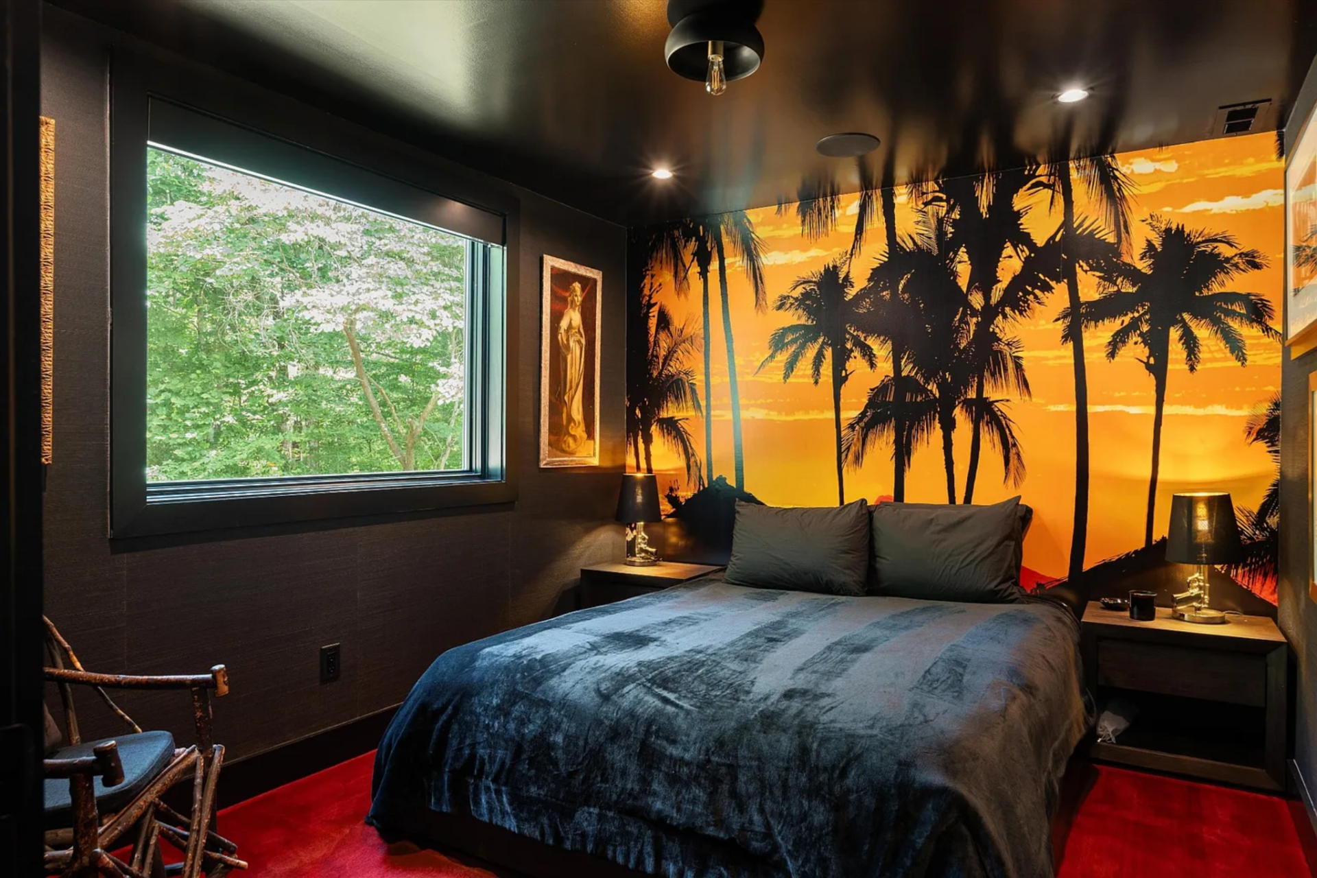 Two separate sleeping areas extend the barn’s usability for guests. One bedroom is surrounded by dark walls and a large-scale mural creating a moody, cocooned environment softened by warm lighting and a single window framing the greenery outside. 