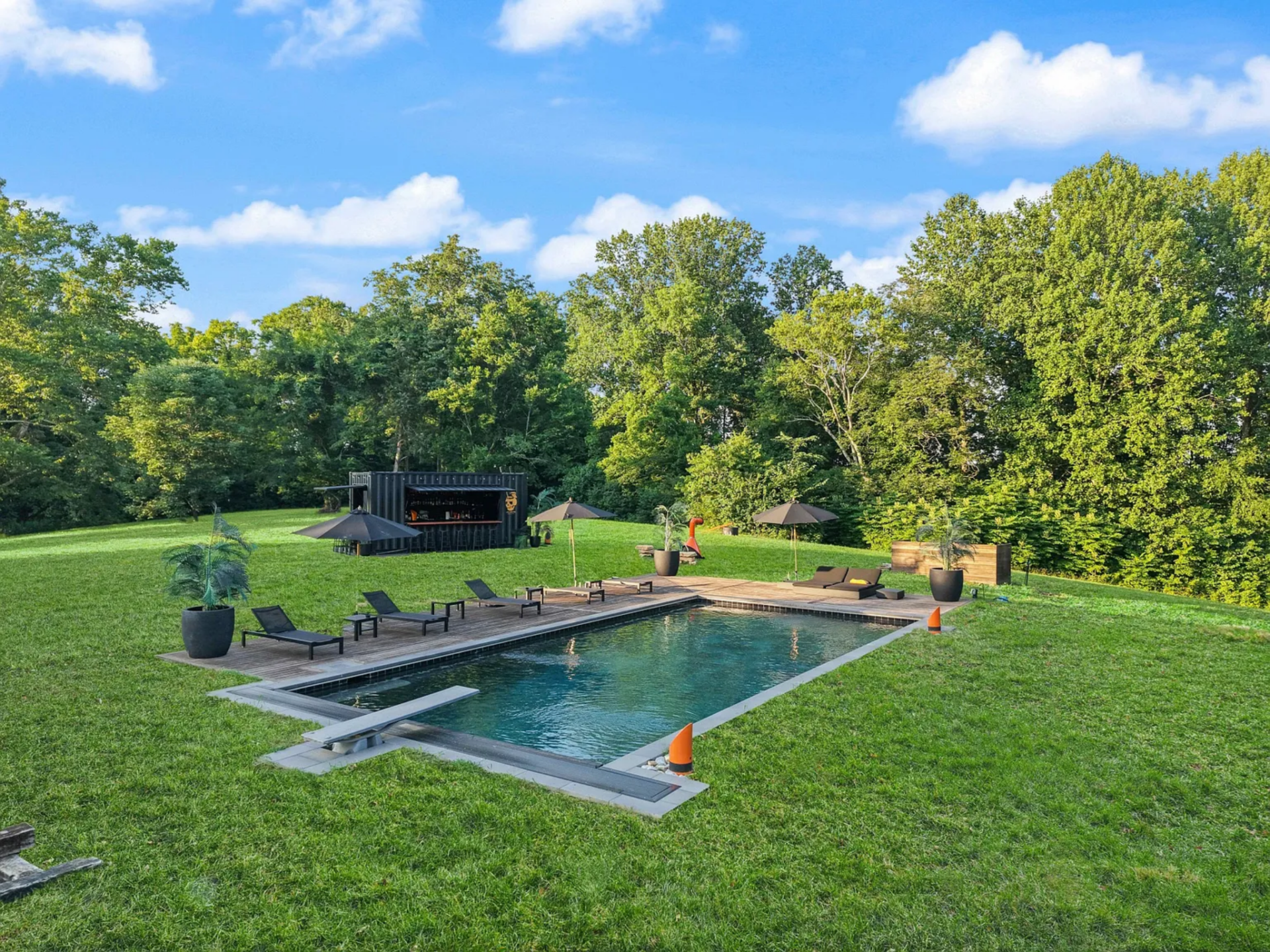 At a higher point on the property, the pool sits within an open lawn, bordered by a wood deck lined with lounge chairs and umbrellas.