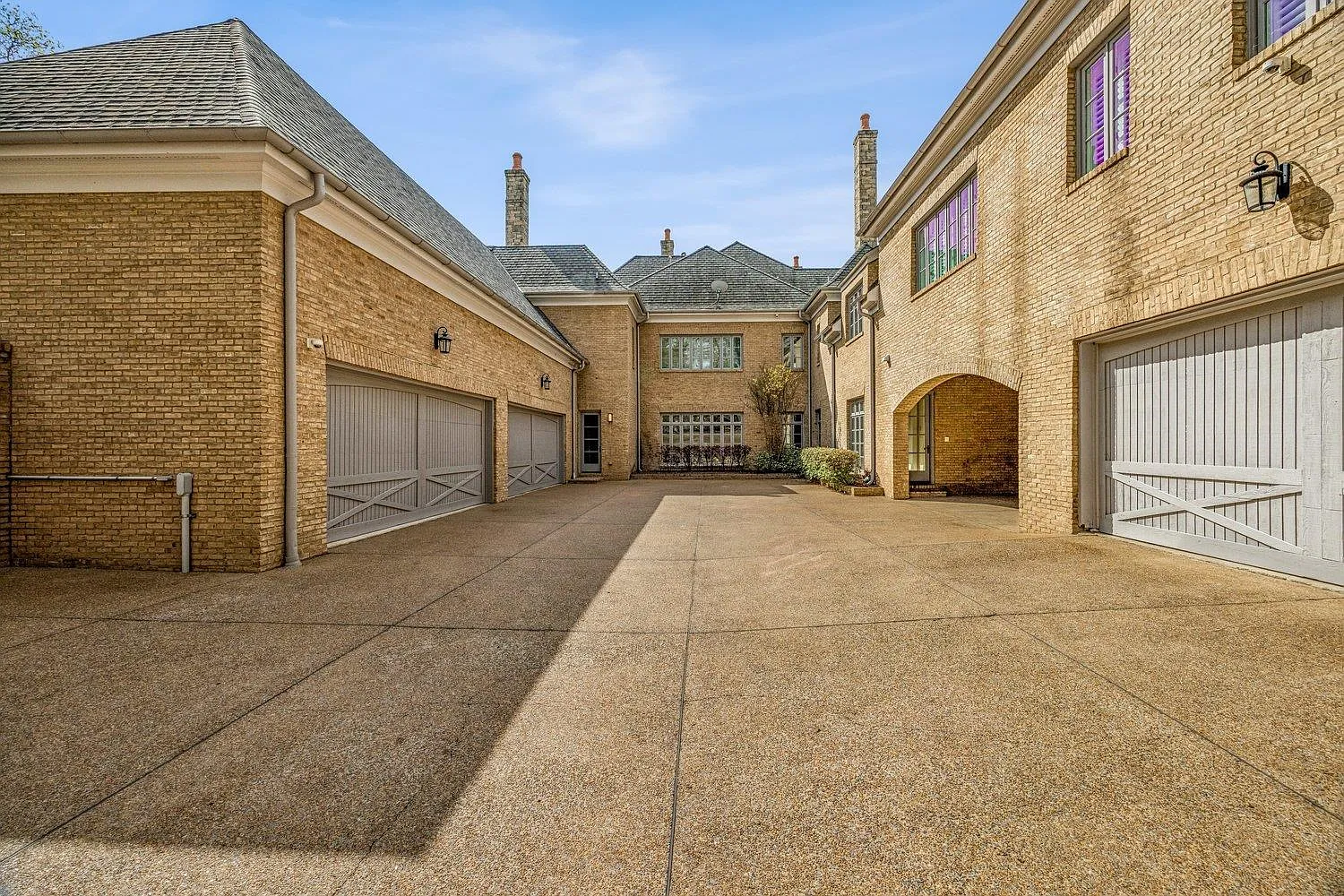 A vertical opening with the house extending on both sides with its brick exterior wrapping around multiple garages on either side.