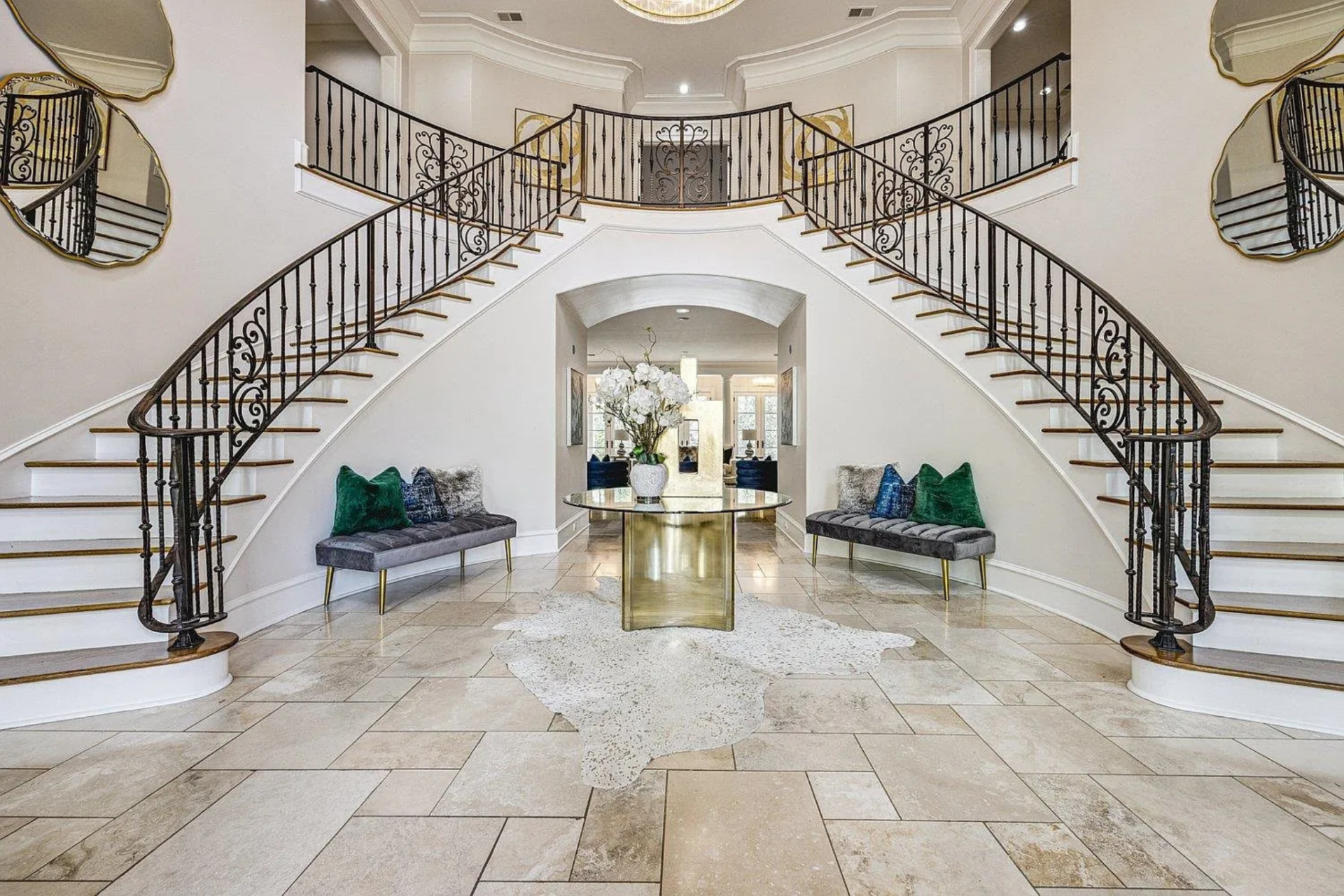 The home opens into a double-height foyer where light stone flooring runs wall to wall and layered crown molding draws the eye upward toward a tiered chandelier.