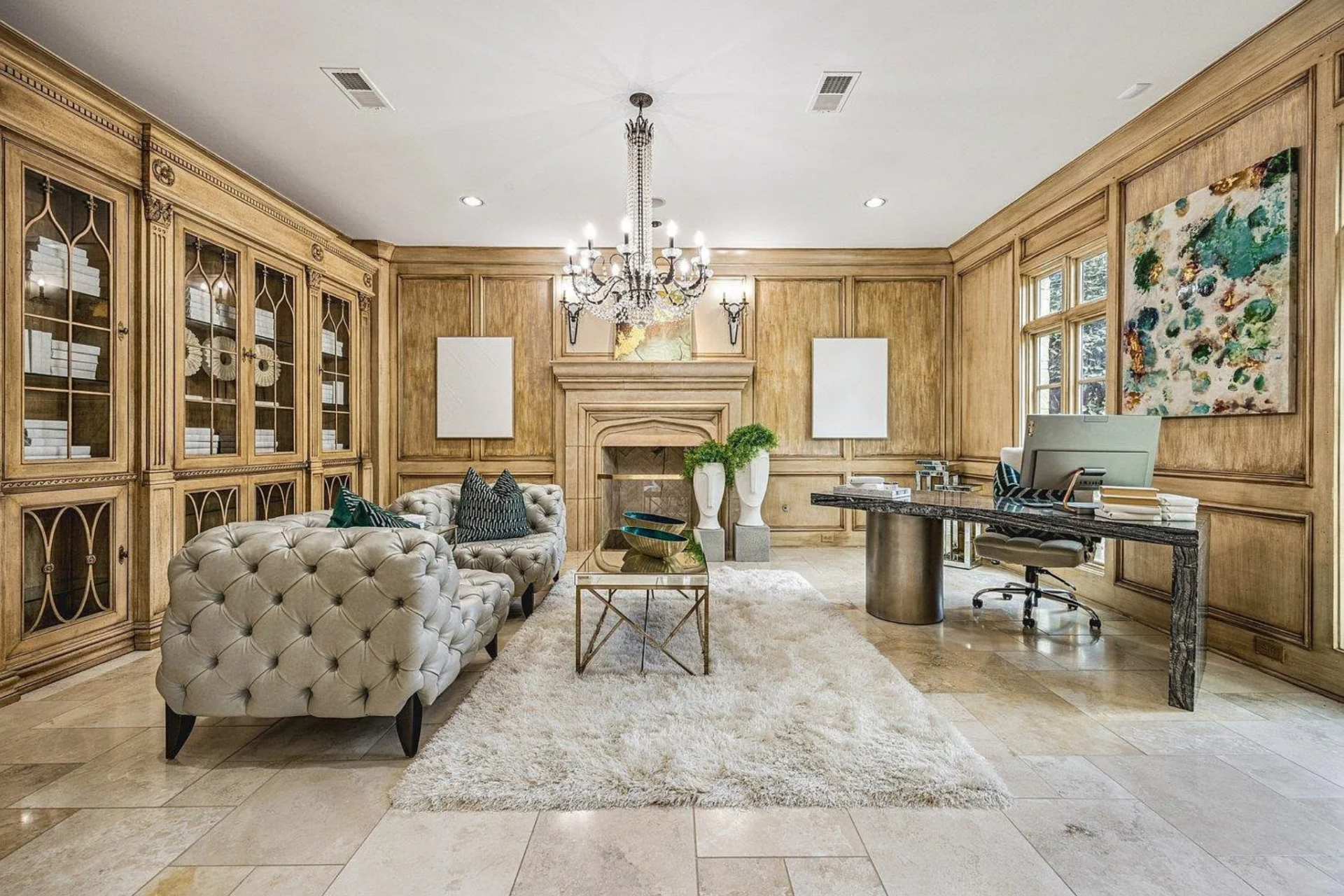 In the center, a pair of tufted lounge chairs and a small glass coffee table create a sitting area across from a dark stone-topped desk.