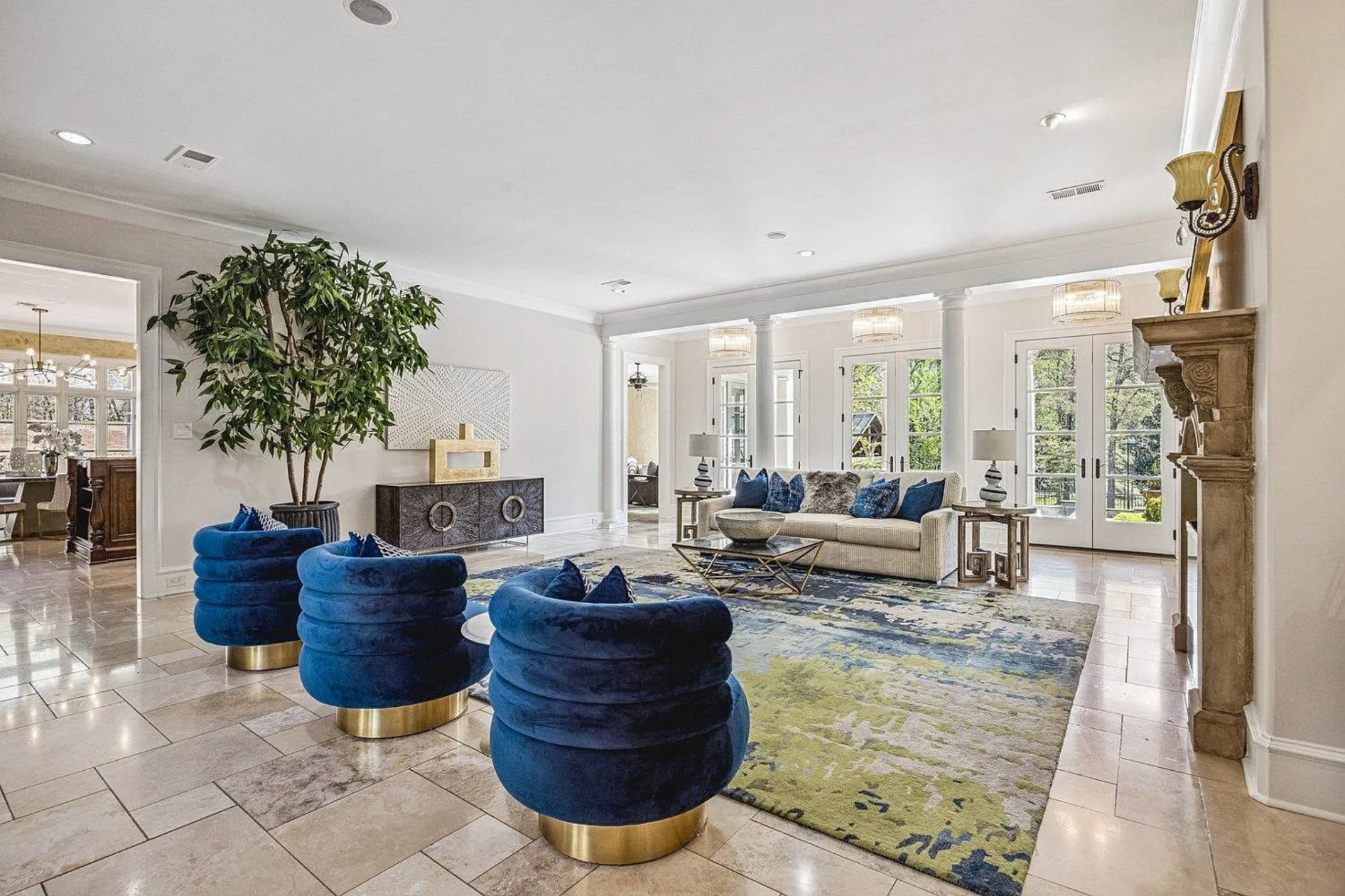 Behind the seating area, a line of tall French doors stretches across the back wall, bringing in natural light and opening the room visually to the outdoor spaces.