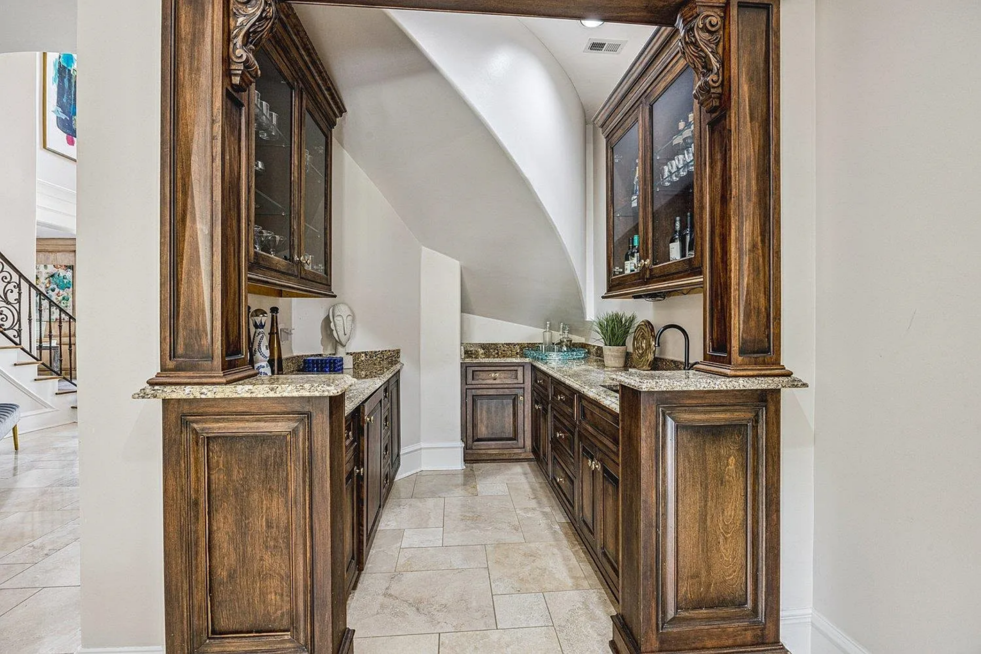 Dark wood cabinetry, stone countertops, and glass-front uppers create a compact but fully functional bar, positioned for entertaining without interrupting the flow of the room.
