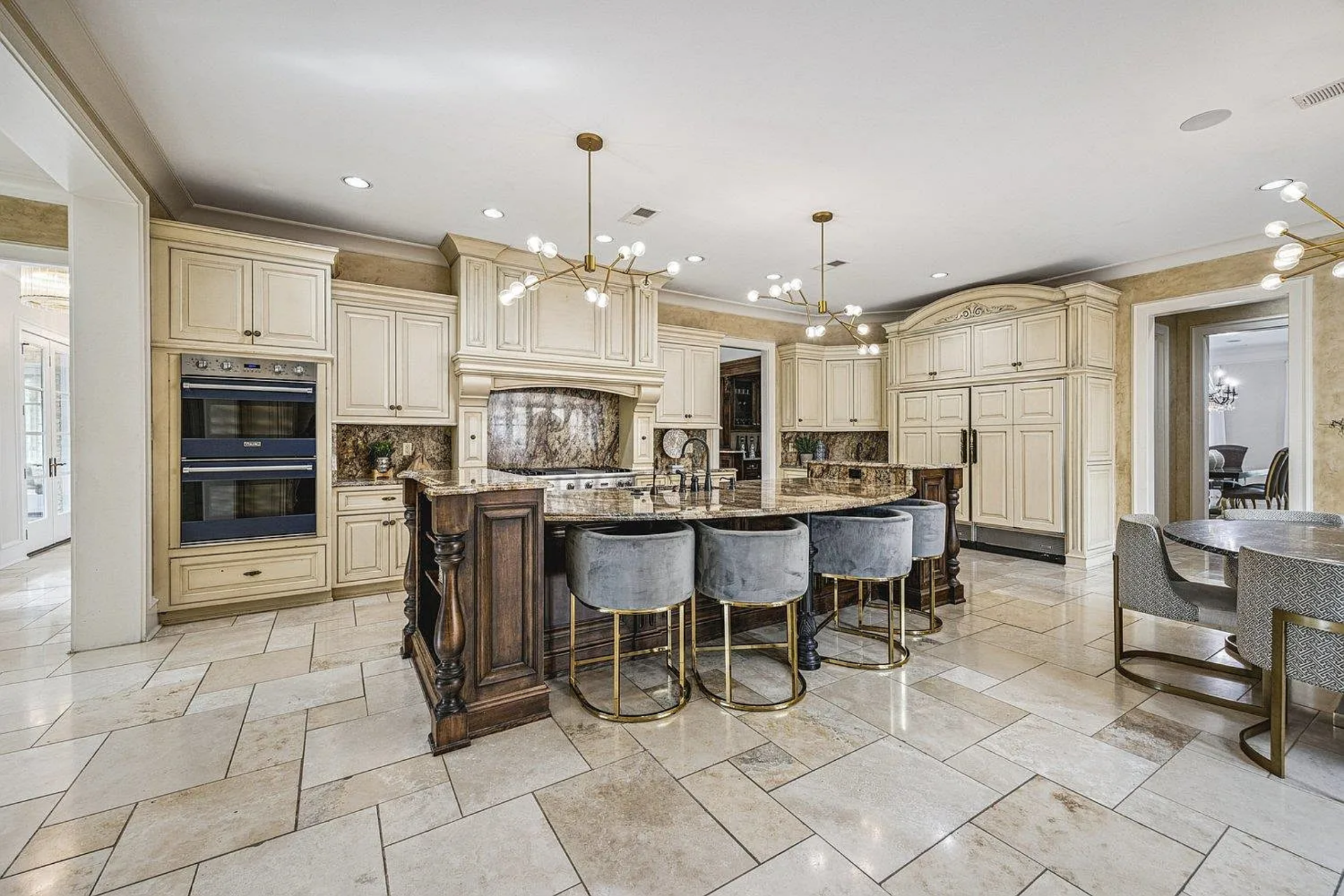 Just around the corner, the kitchen has cream-toned cabinetry wrapping the perimeter, paired with detailed millwork and a carved range hood that frames the cooktop against a slab backsplash.