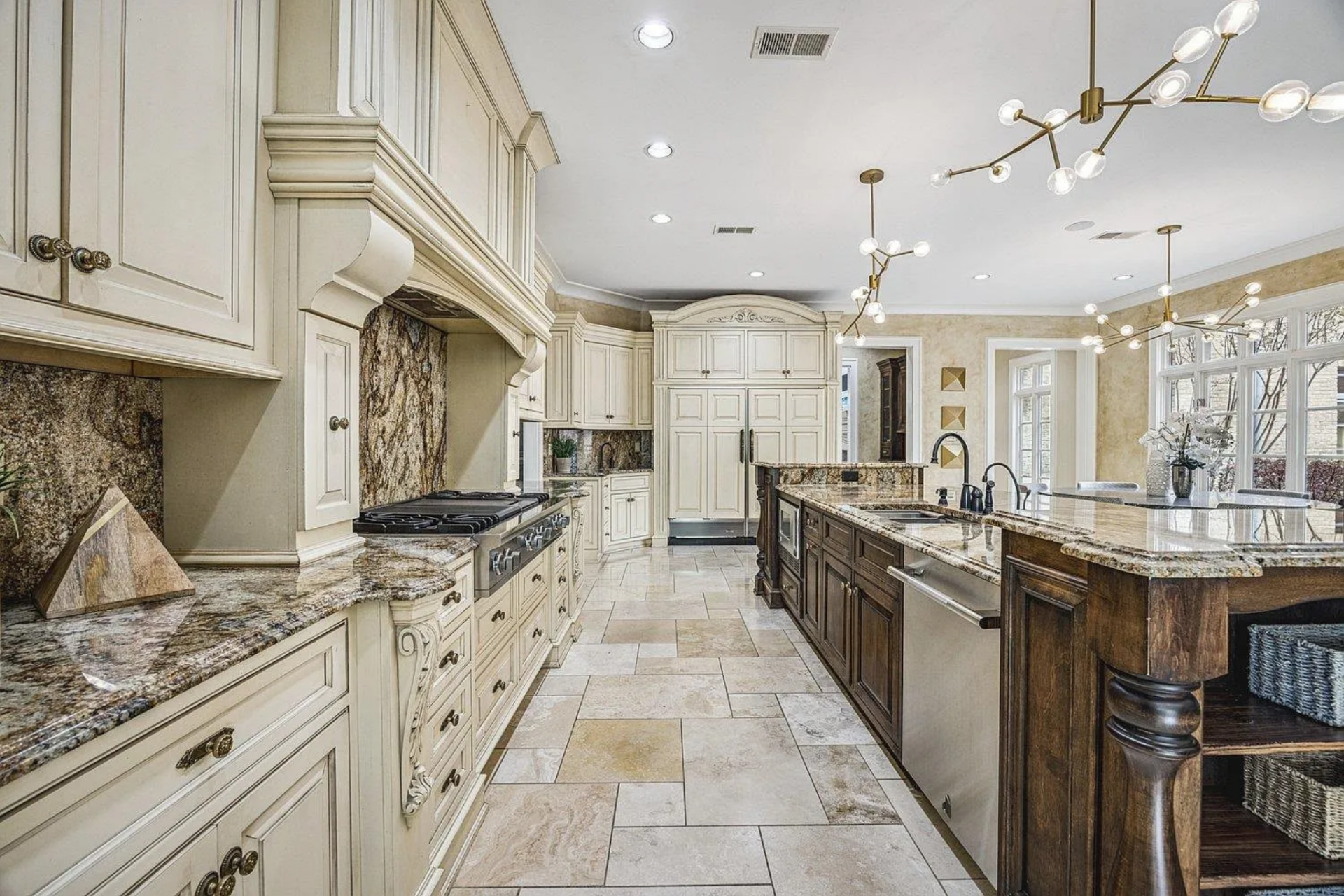 At the center, a large island is lined with a darker wood base and granite countertops, fitted with an integrated sink and lined with upholstered barstools for casual seating.