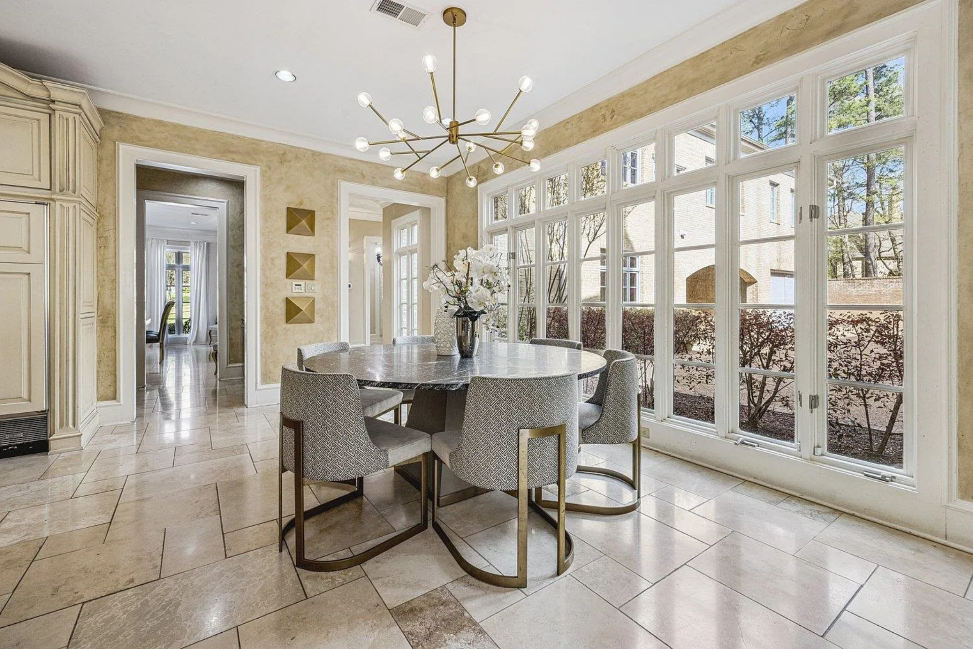 Extending off the kitchen, the breakfast nook consists of a round table surrounded by six upholstered chairs along a wall of tall, gridded windows that bring in natural light.