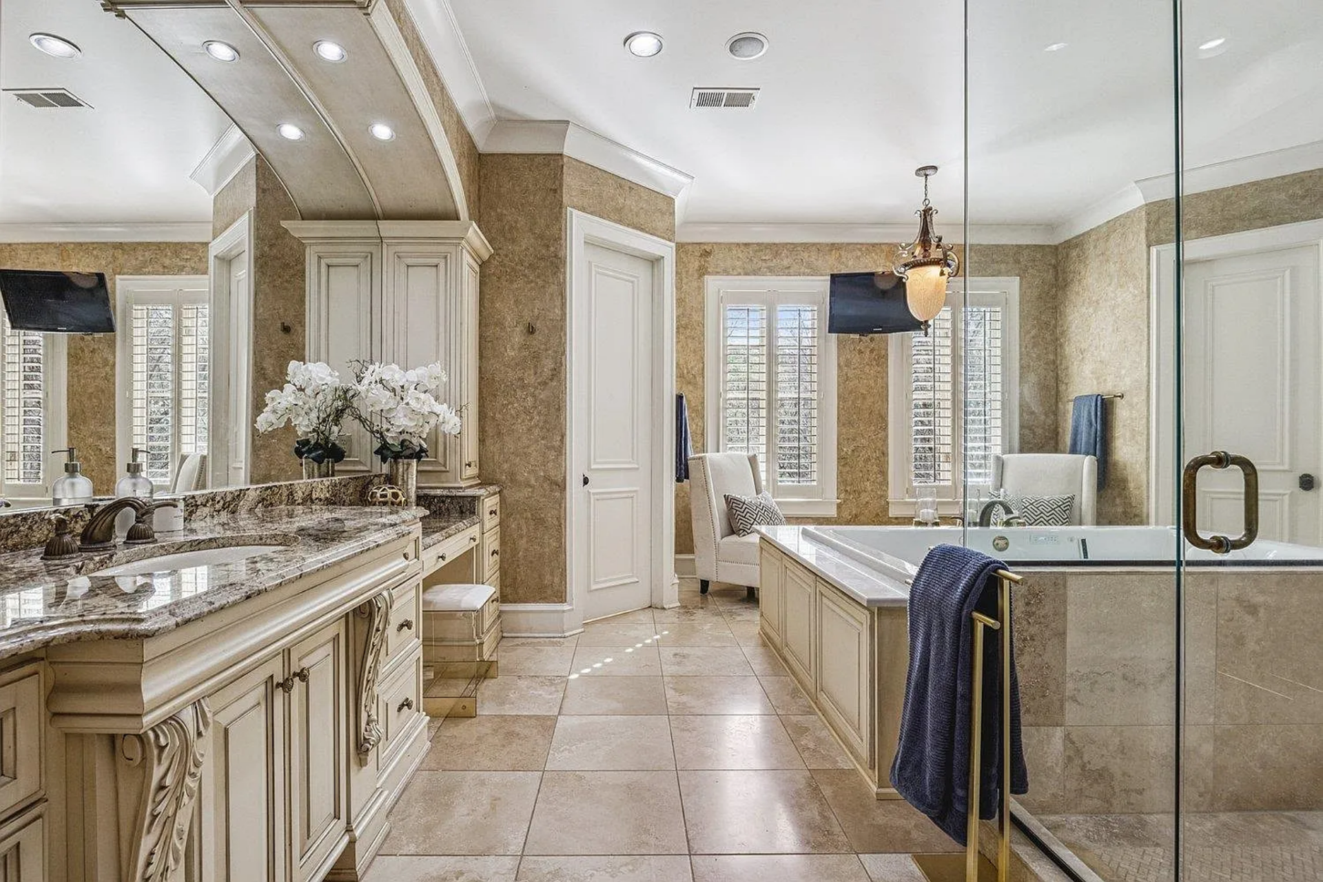 The bathroom continues the same level of detail, with stone flooring, built-in cabinetry, and a large central soaking tub set within a raised surround.