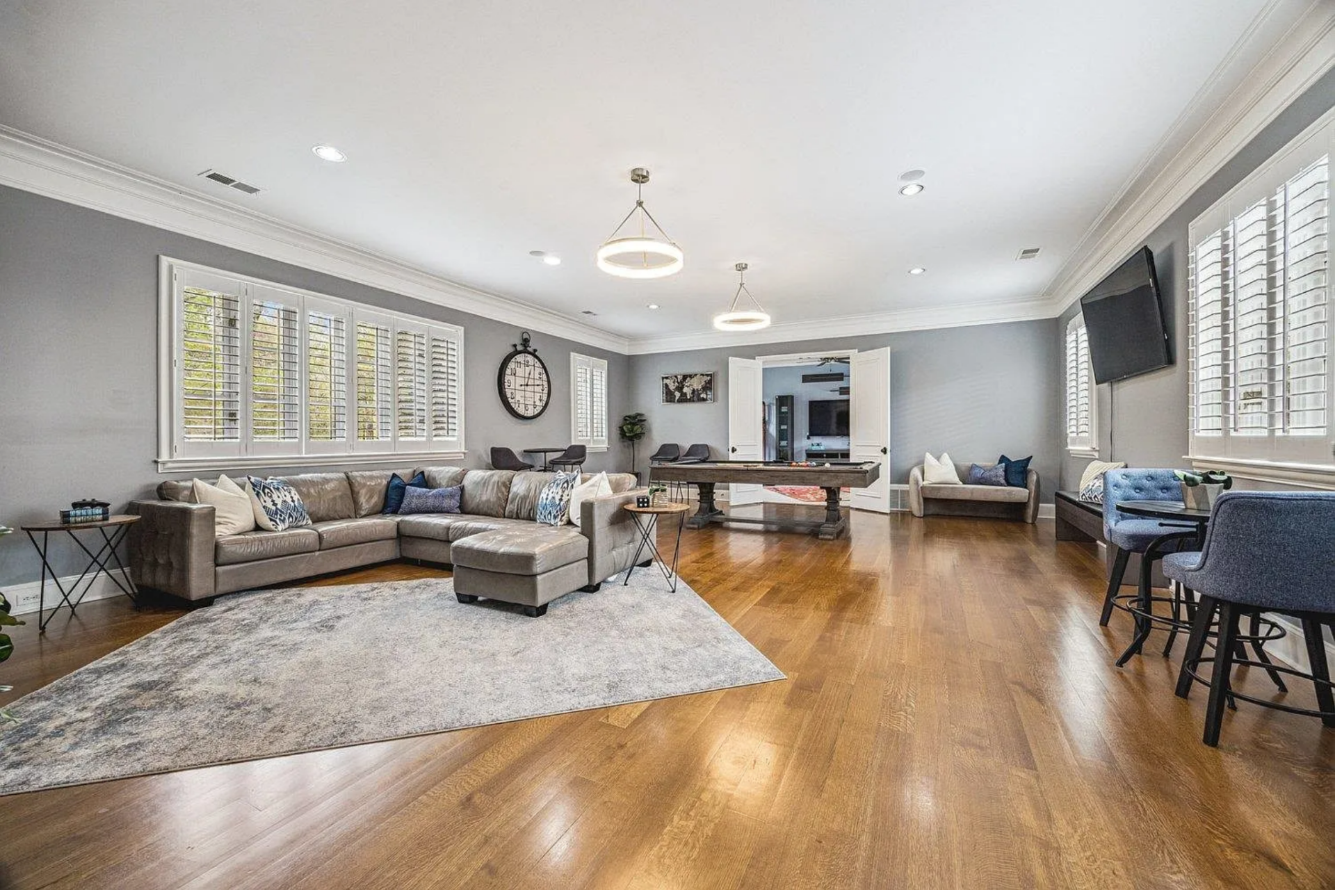 The expansive game room features a large sectional seating area, a billiards table, and a mounted flatscreen TV, creating zones for both activity and relaxation.