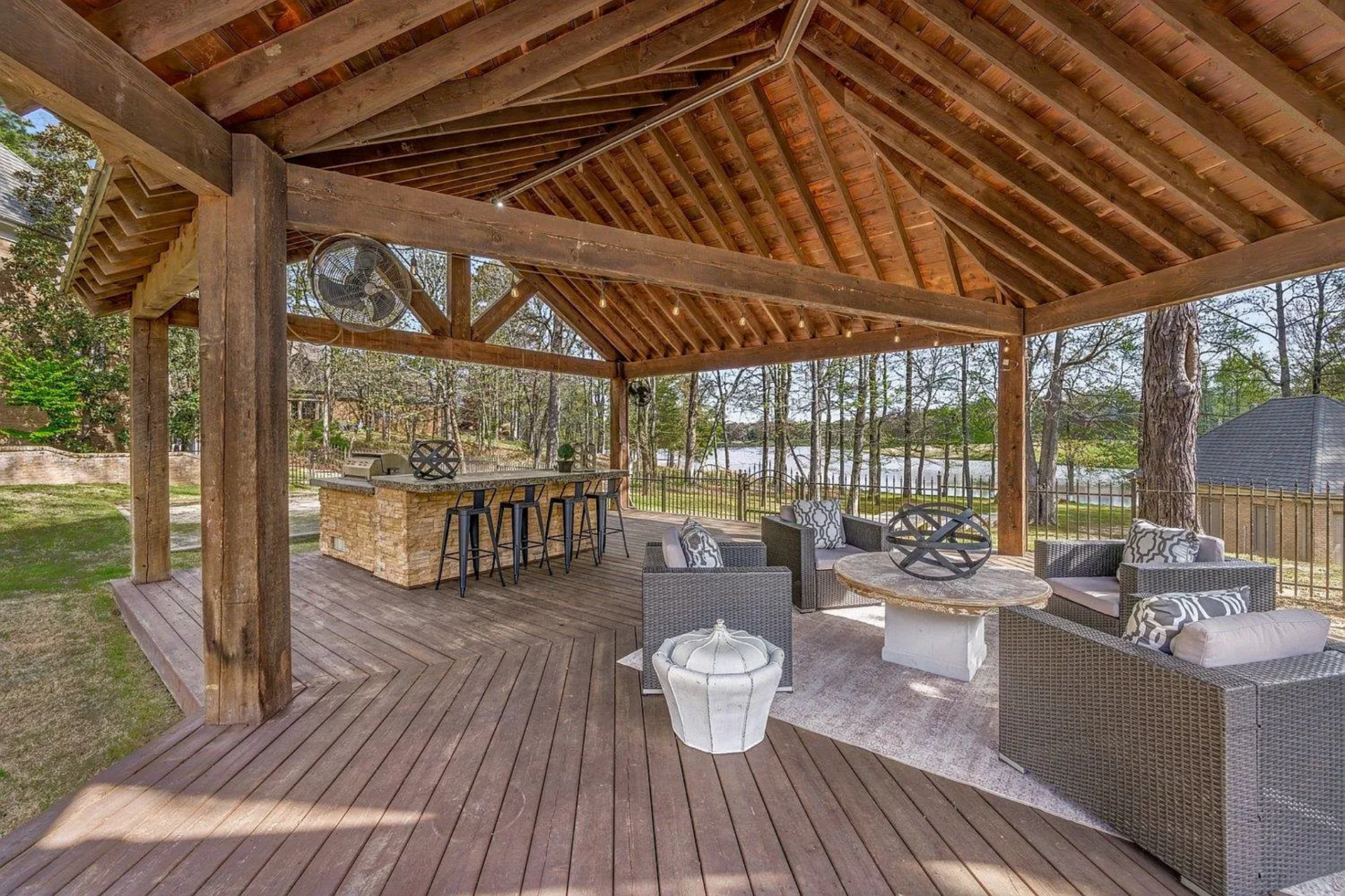 Beneath it, a fully equipped outdoor kitchen and bar seating area allow for easy hosting, while adjacent lounge seating creates a comfortable setting for conversation overlooking the pool.